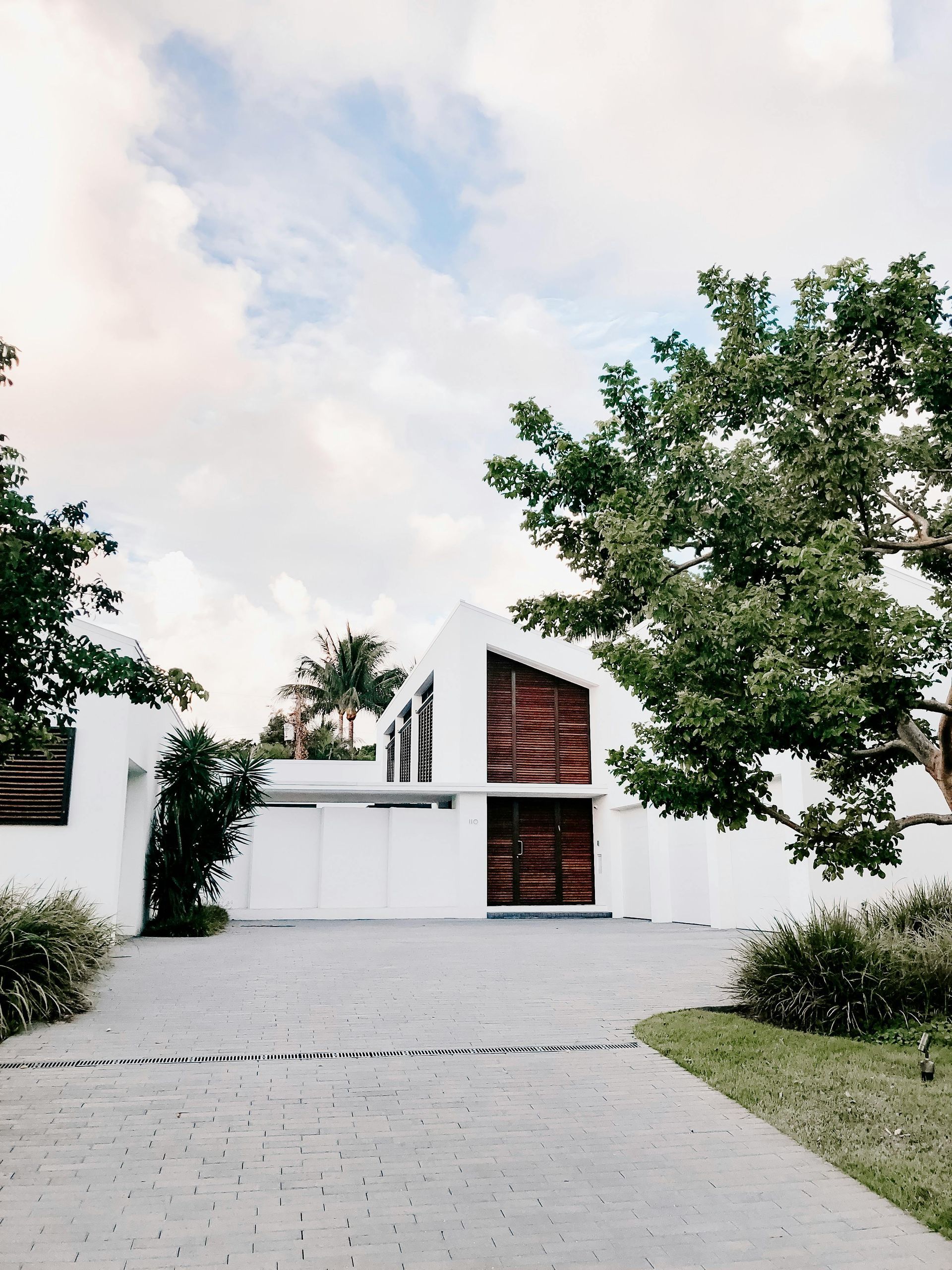 White modern building with wood accents and trees, cloudy sky.