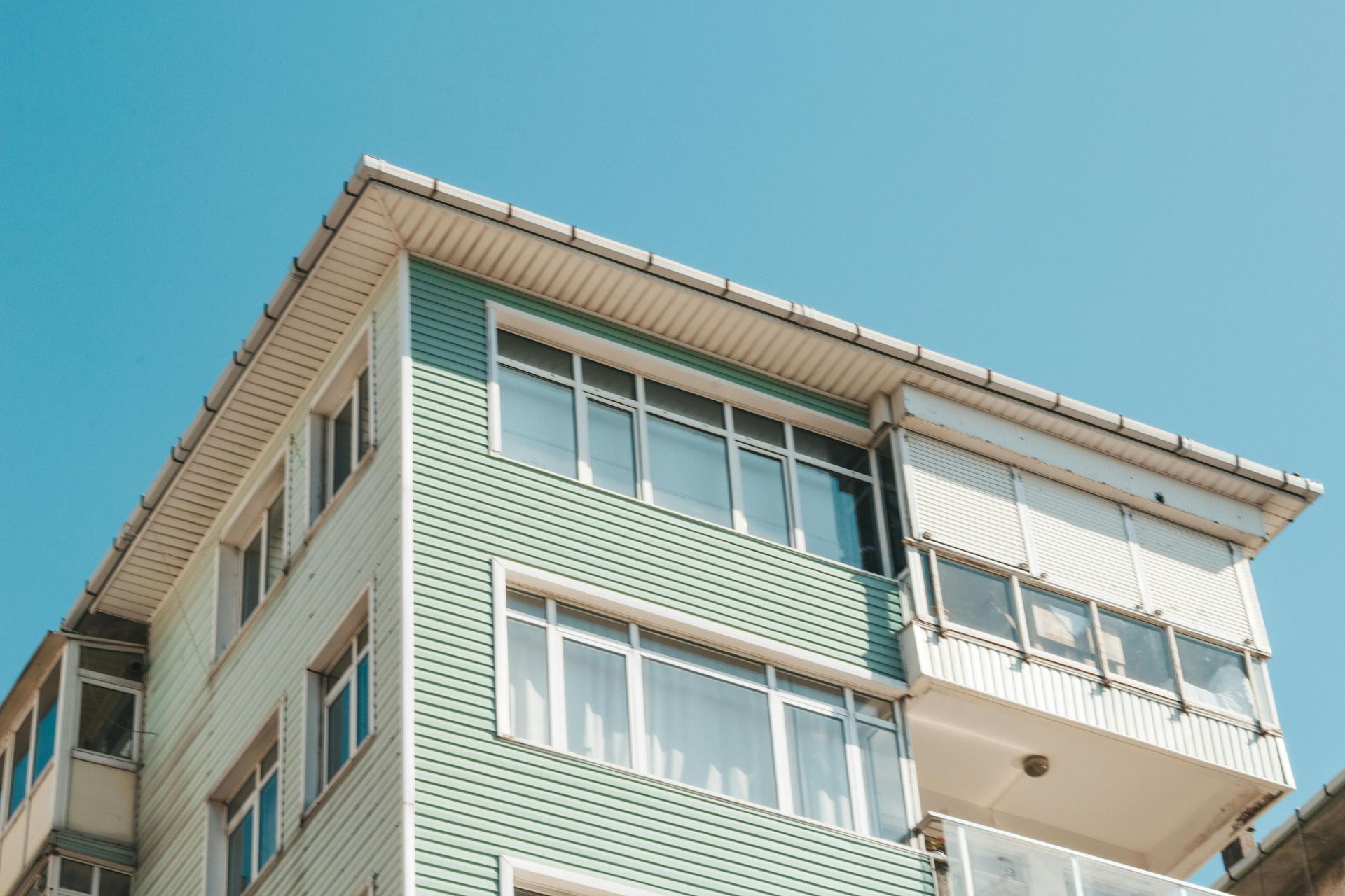 Three-story building with teal siding and multiple windows against a clear blue sky.