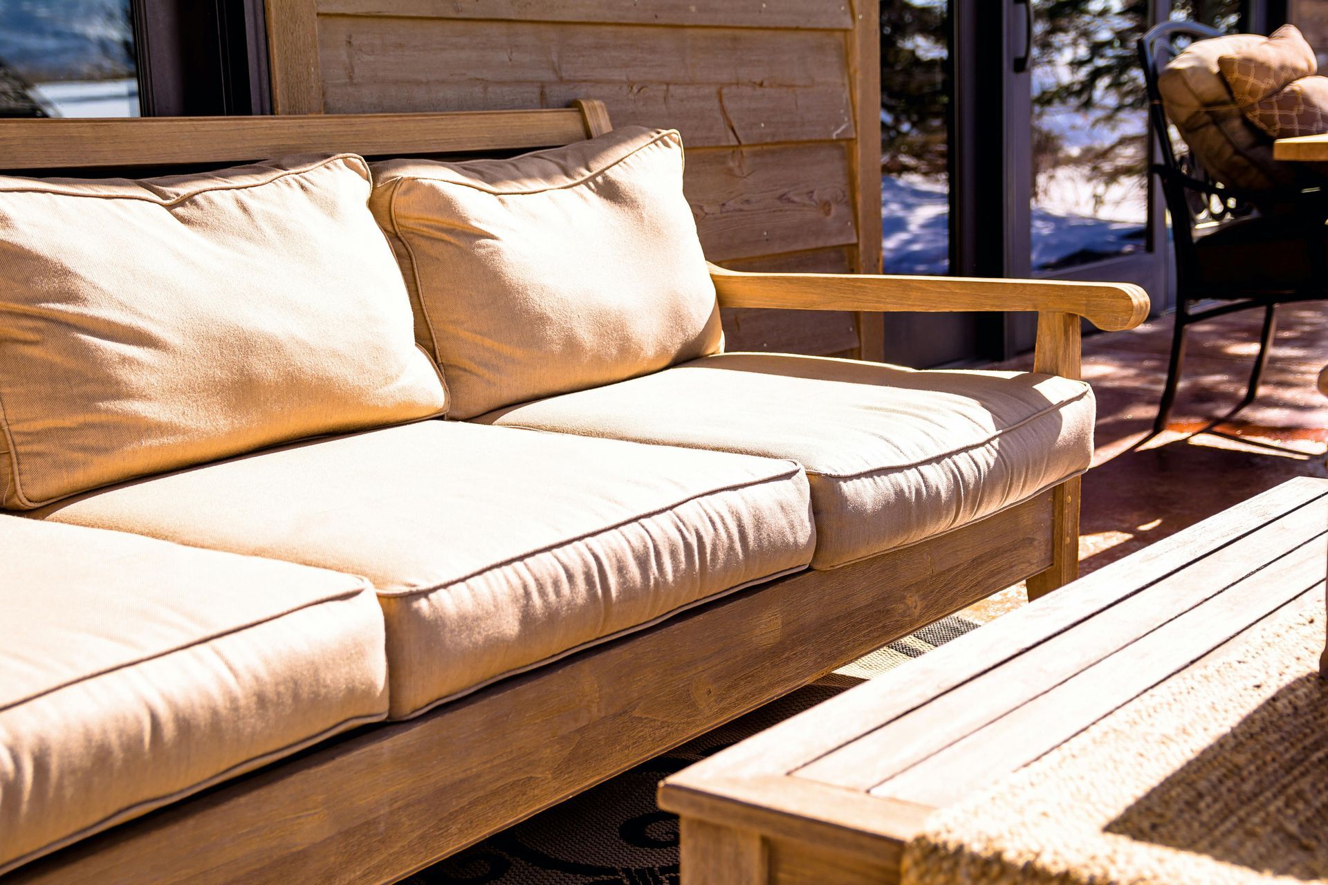 Outdoor wooden sofa with beige cushions on a deck. Sunny setting.