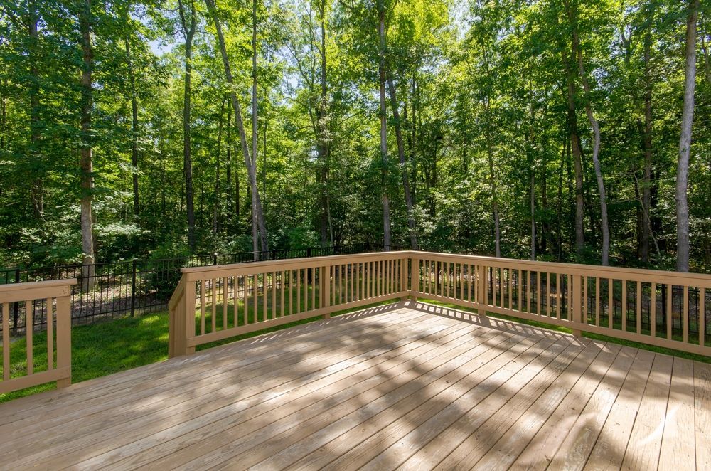 Wooden deck surrounded by wooden railing, overlooking a lush green forest on a sunny day.