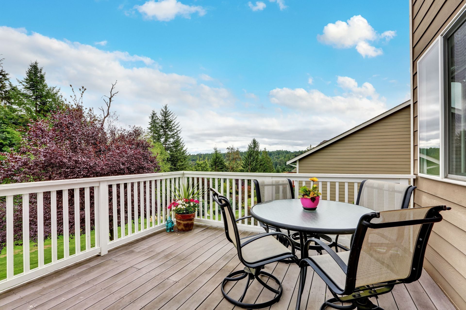 Wooden deck with table and chairs, overlooking a green landscape under a blue sky.