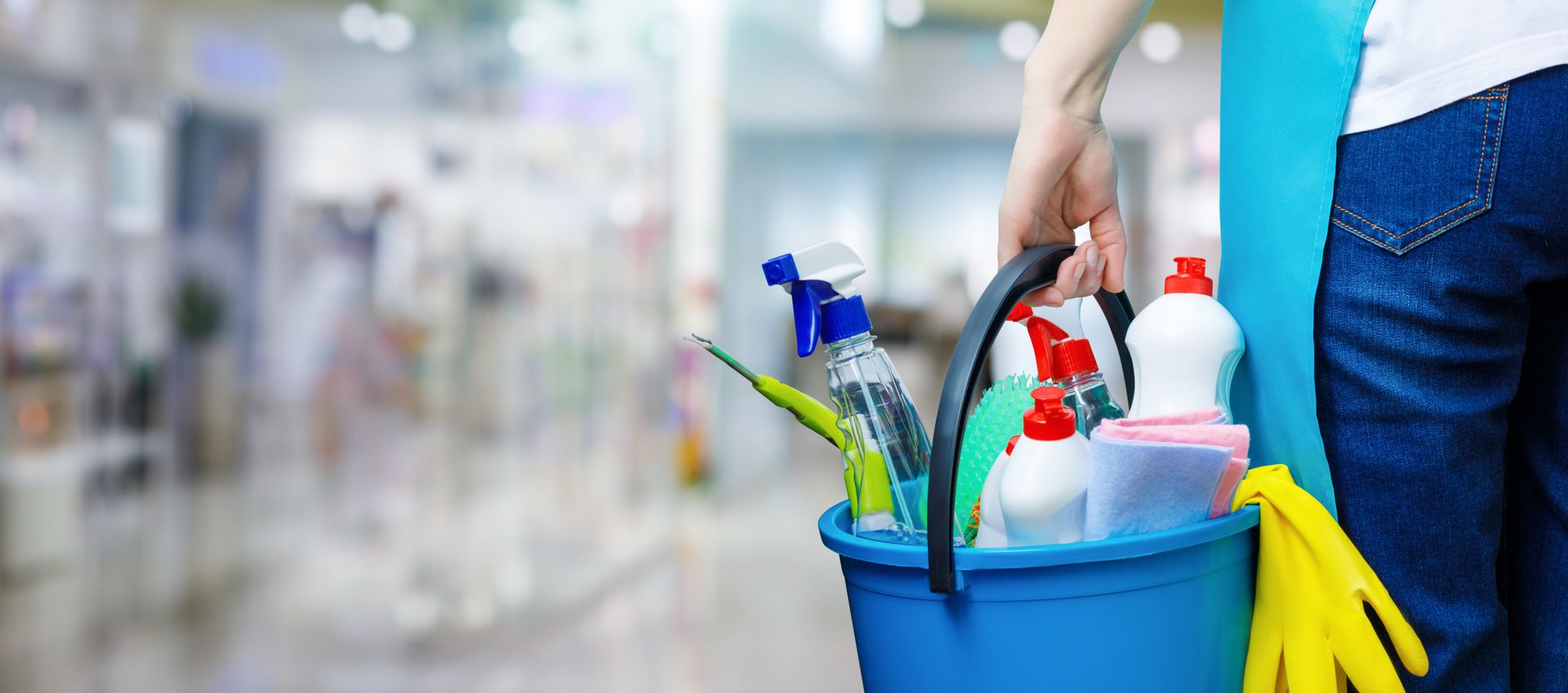 A woman is holding a blue bucket filled with cleaning supplies.