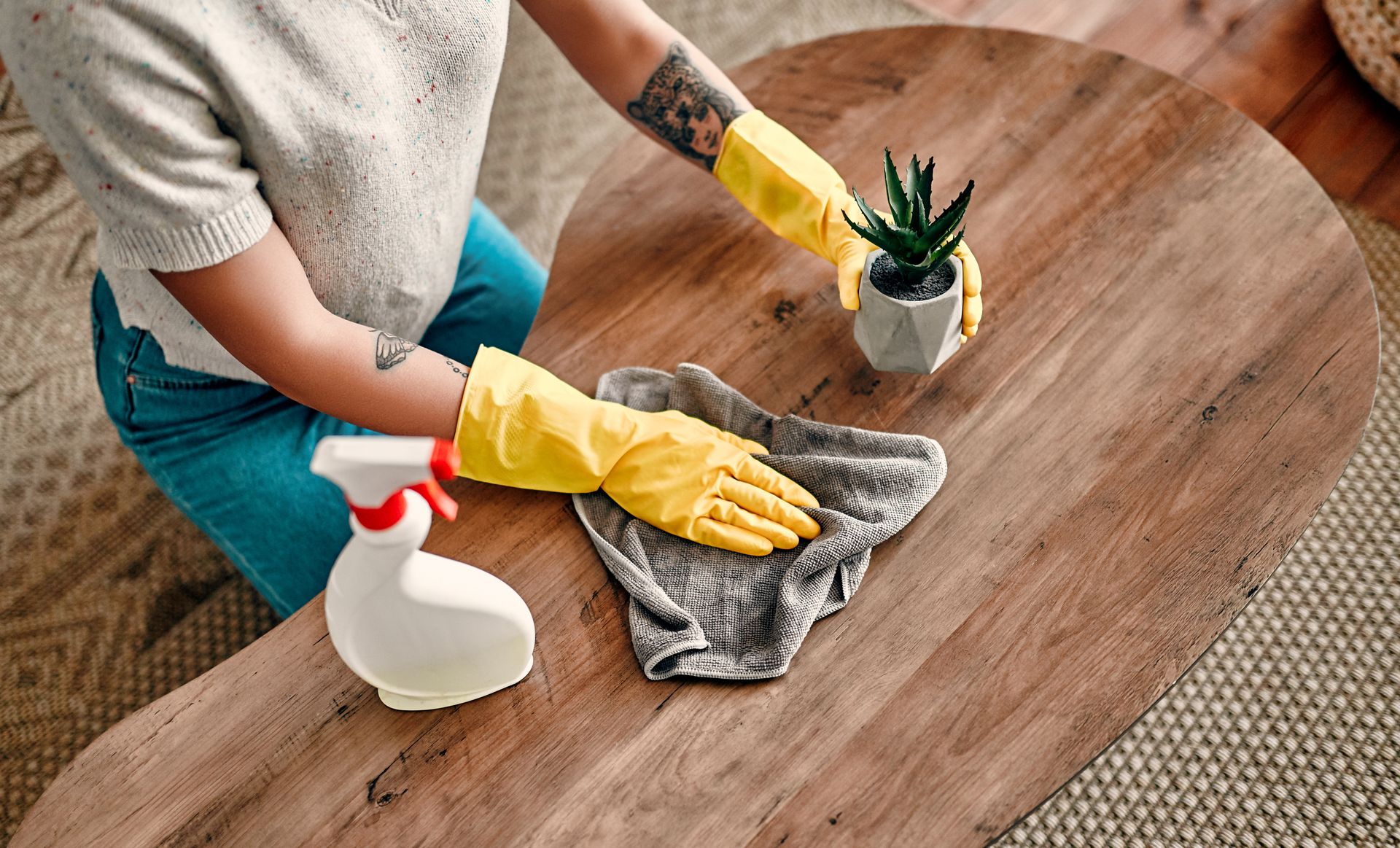 A woman wearing yellow gloves is cleaning a wooden table.