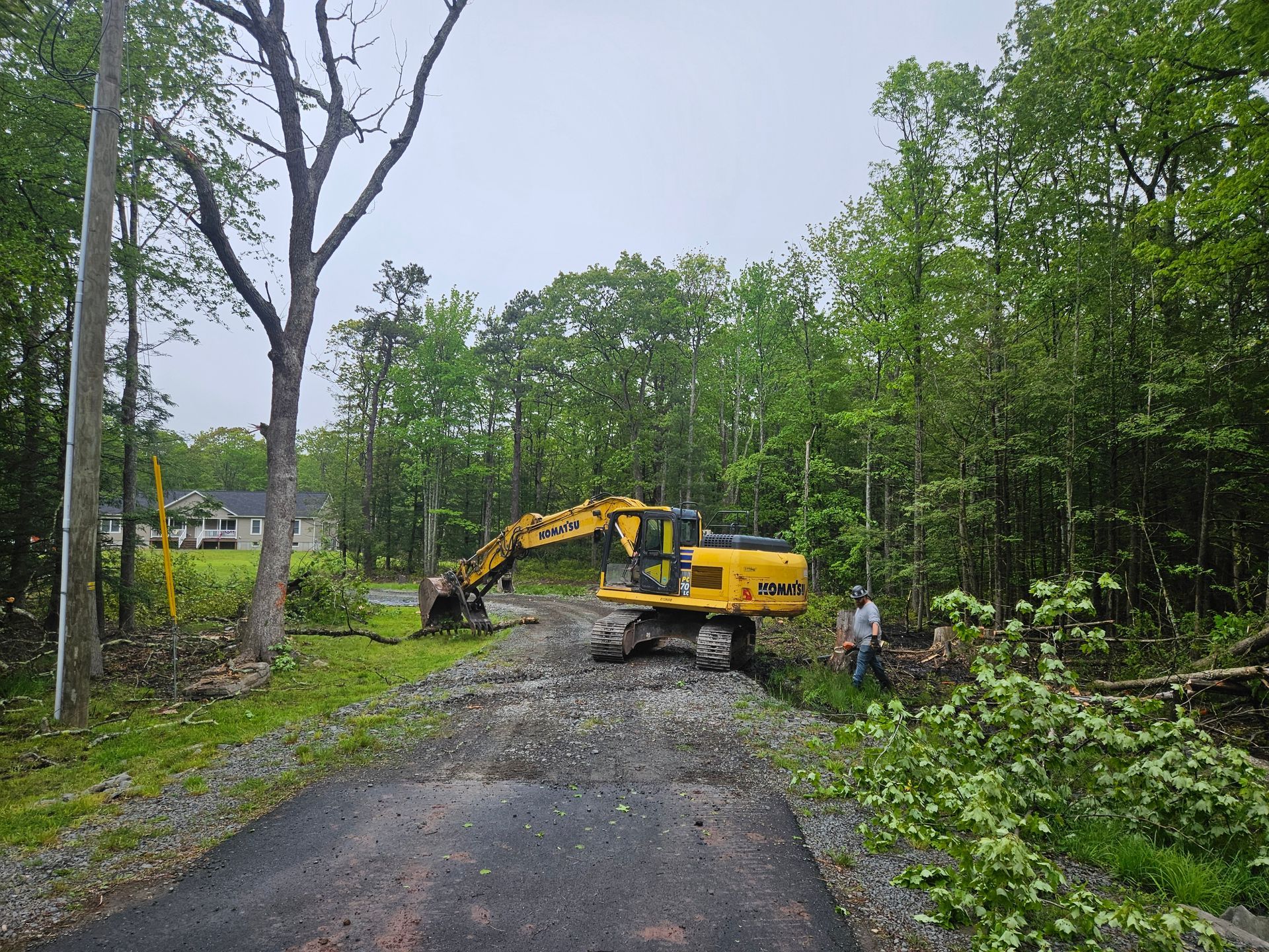 A yellow excavator is working on a road in the woods