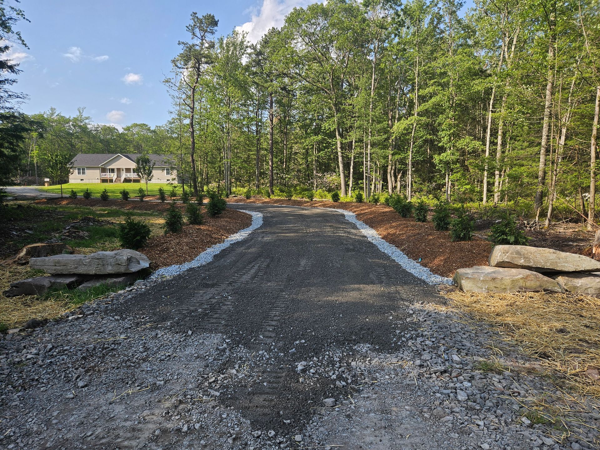 A gravel road going through a forest with a house in the background.