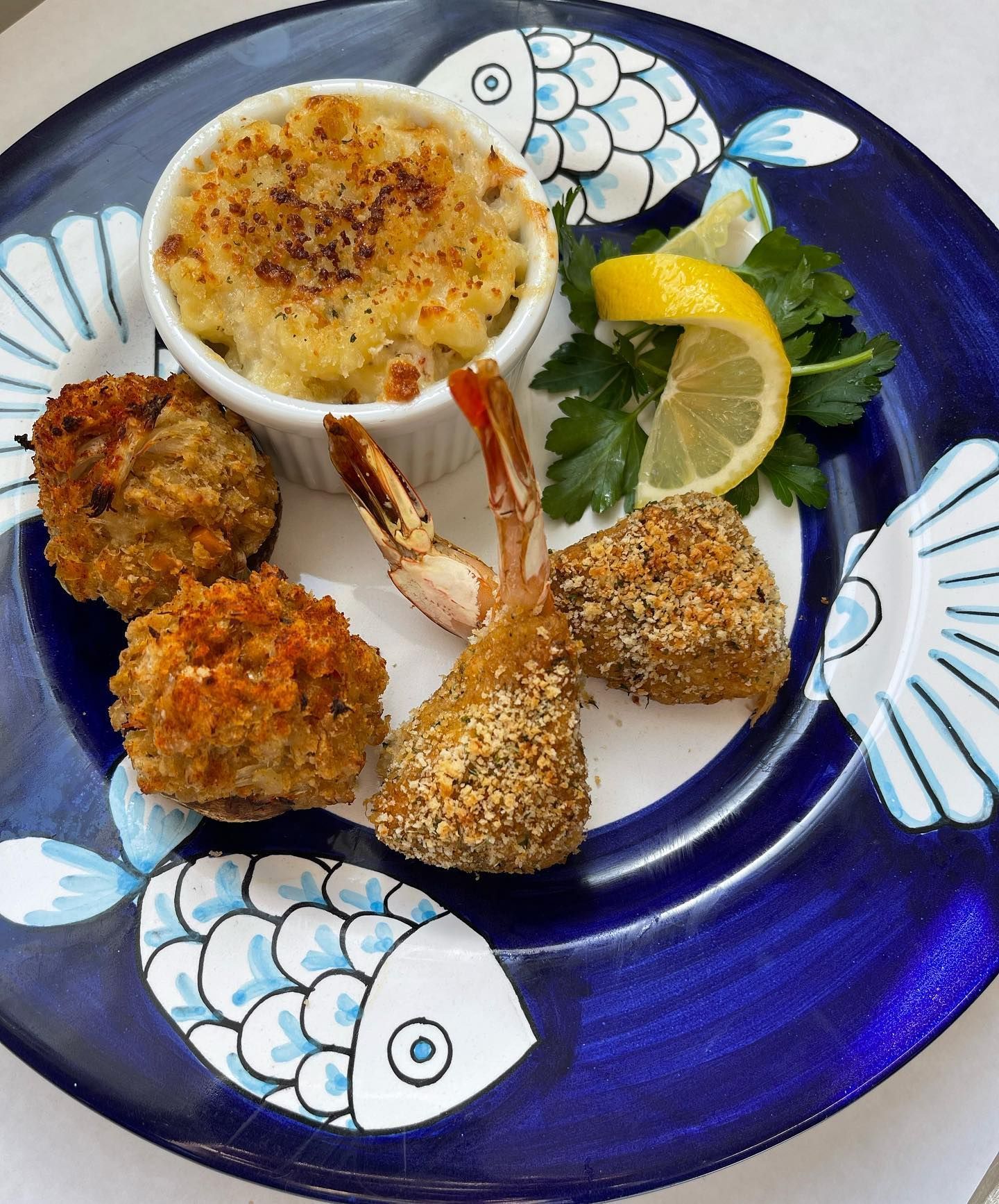 Seafood appetizer plate: mac and cheese, breaded shrimp, scallops, and lemon garnish on a blue fish-patterned plate.