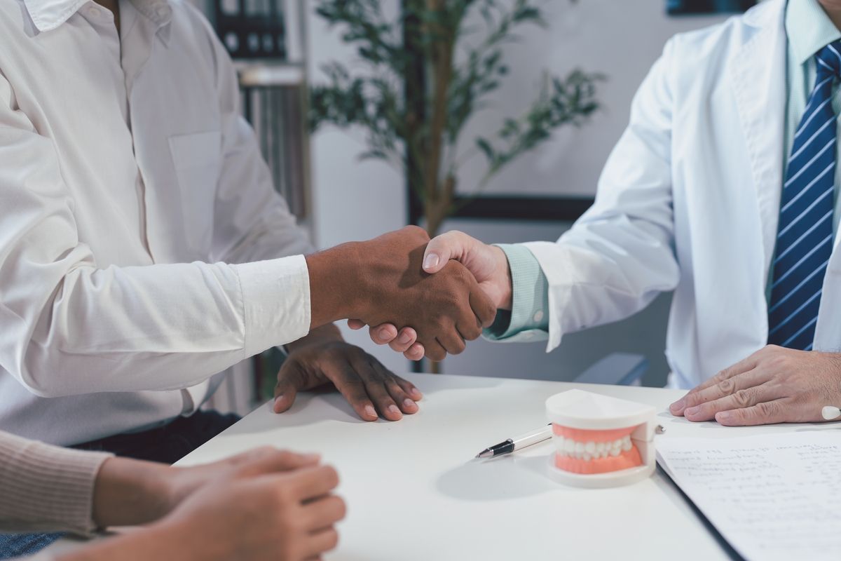 Two people in office attire shaking hands across a desk with documents and a coffee cup nearby