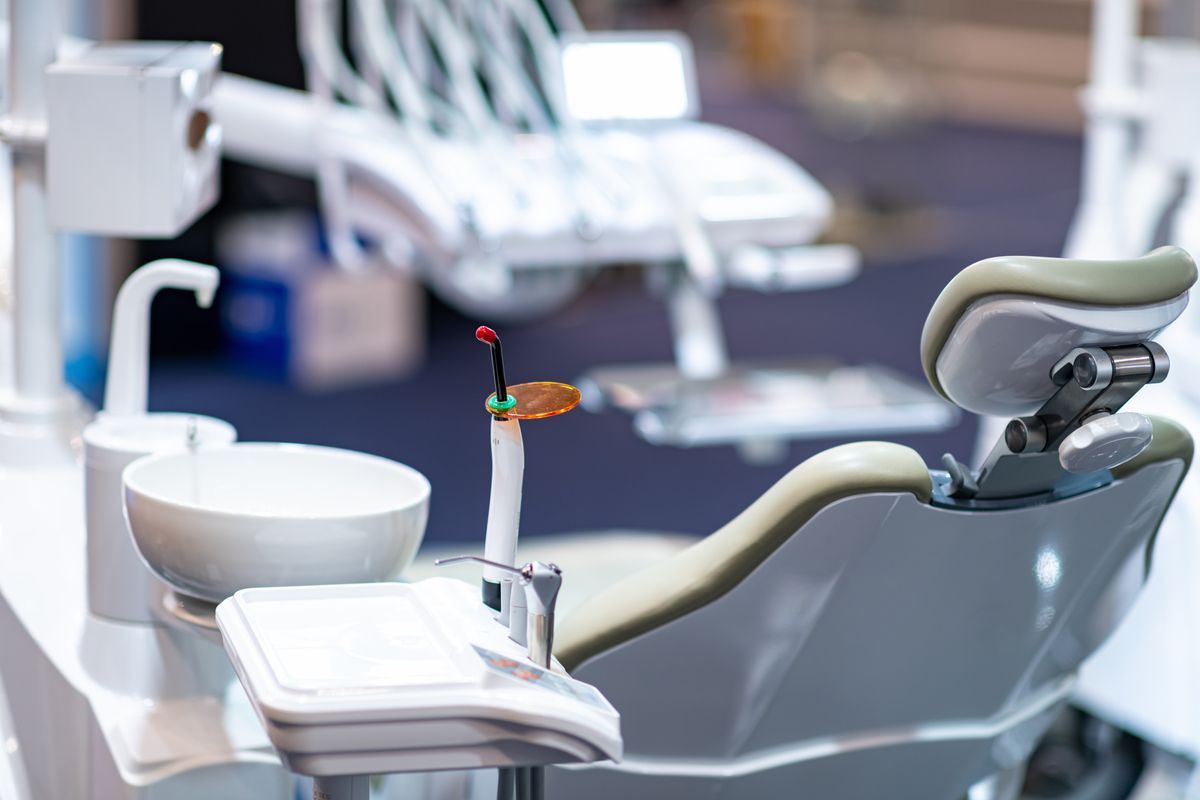 Dental chair and equipment in a clinic, with a sink and tools beside the patient seat.