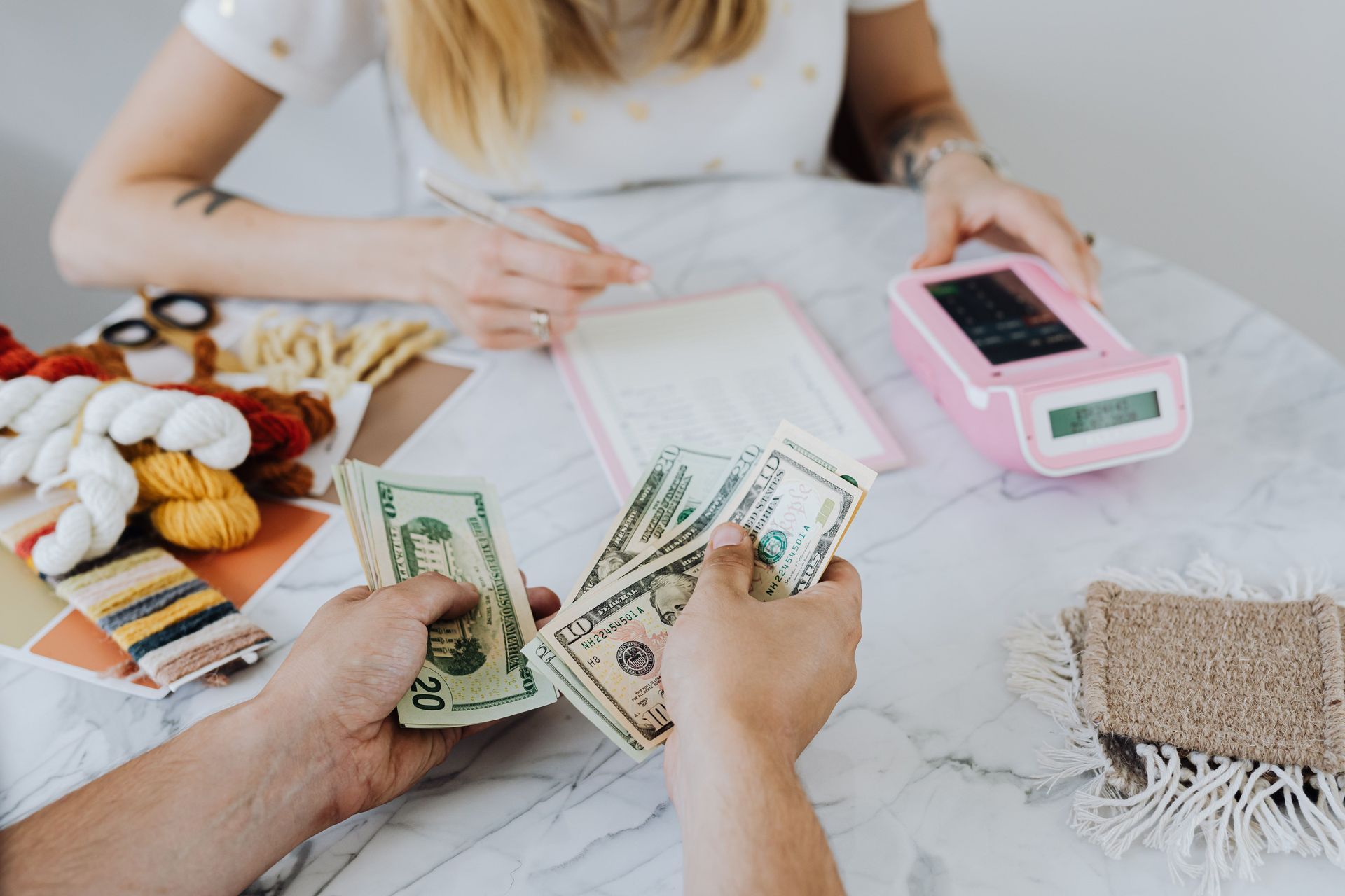 Two people sitting at a table with documents and money, going over finances and details