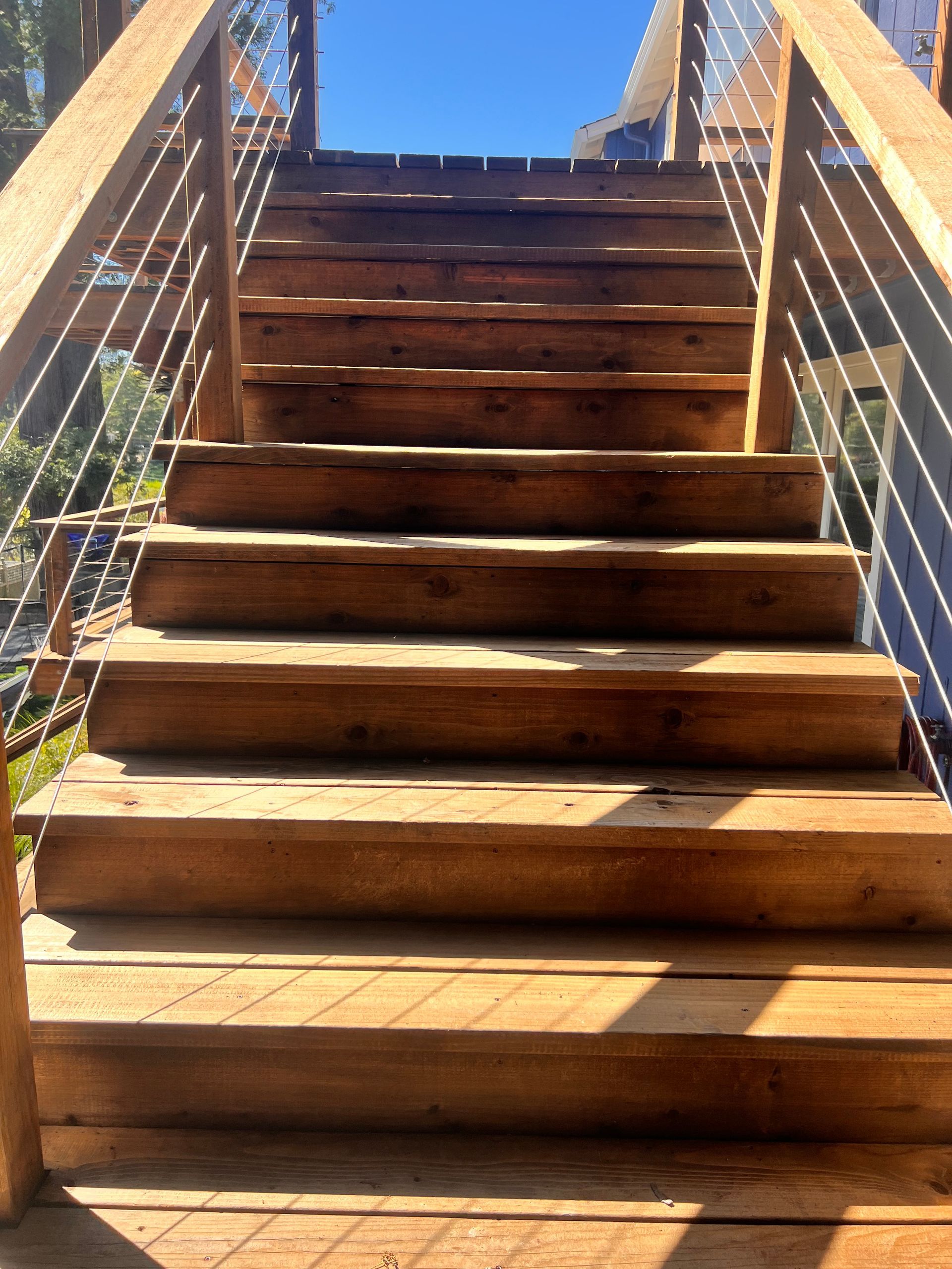 Wooden outdoor staircase with metal railings, viewed from the bottom in bright sunlight