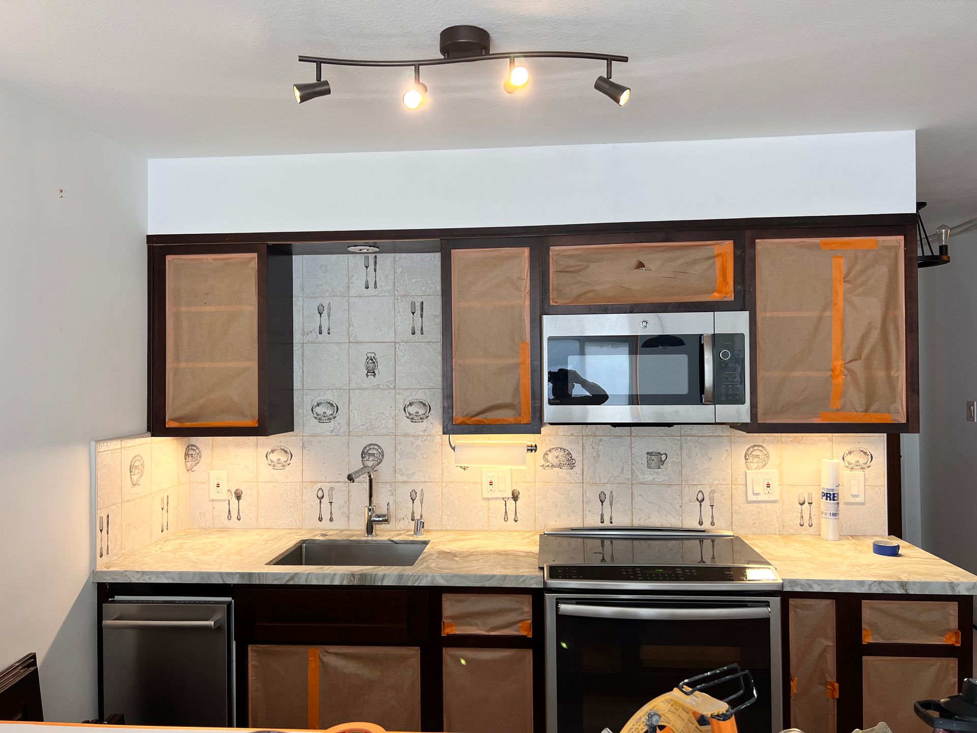 Modern kitchen with dark cabinets, white tile backsplash, stainless appliances, and ceiling track light fixtures