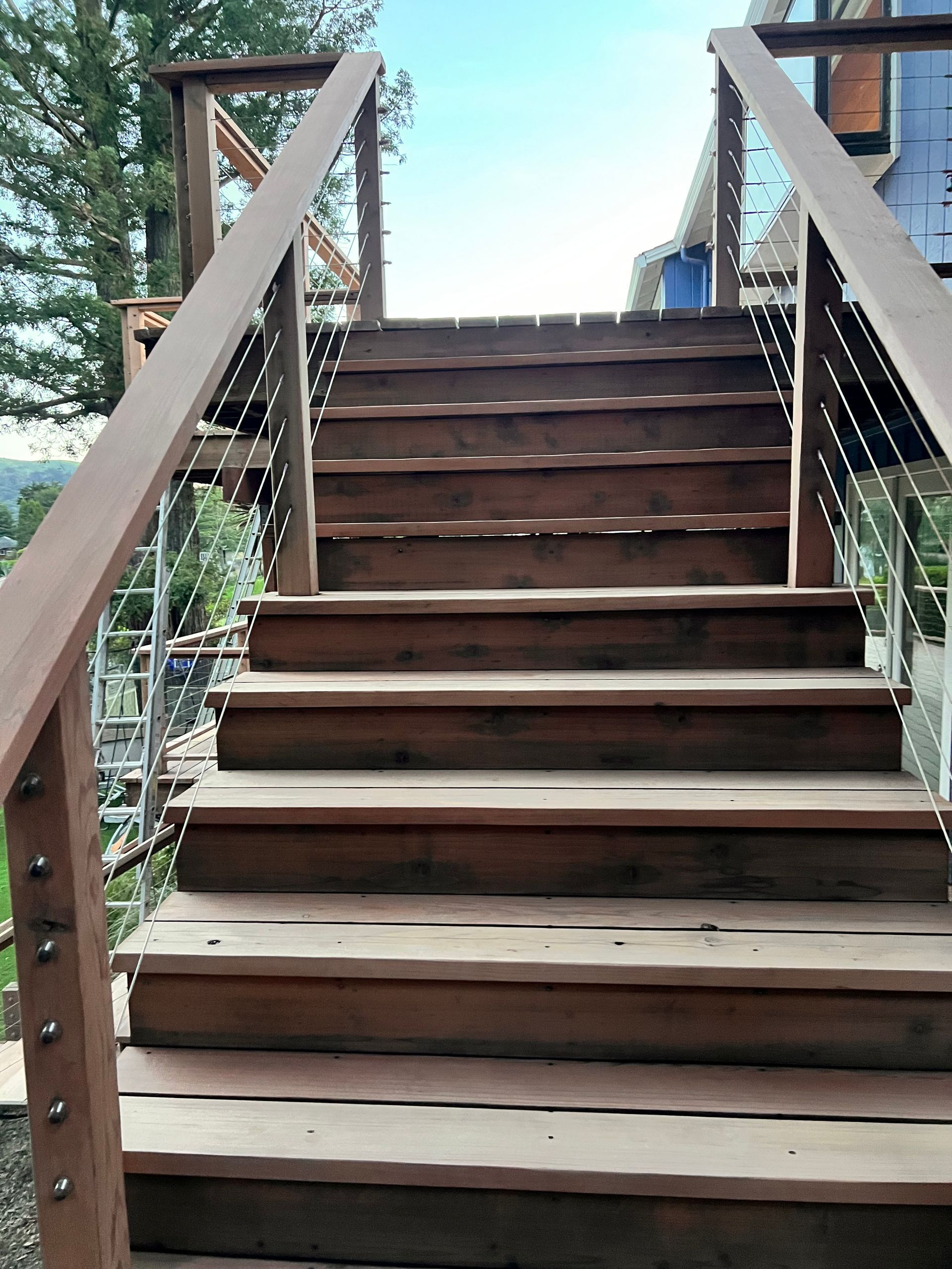 Wooden outdoor staircase with brown railings leading up between buildings and trees