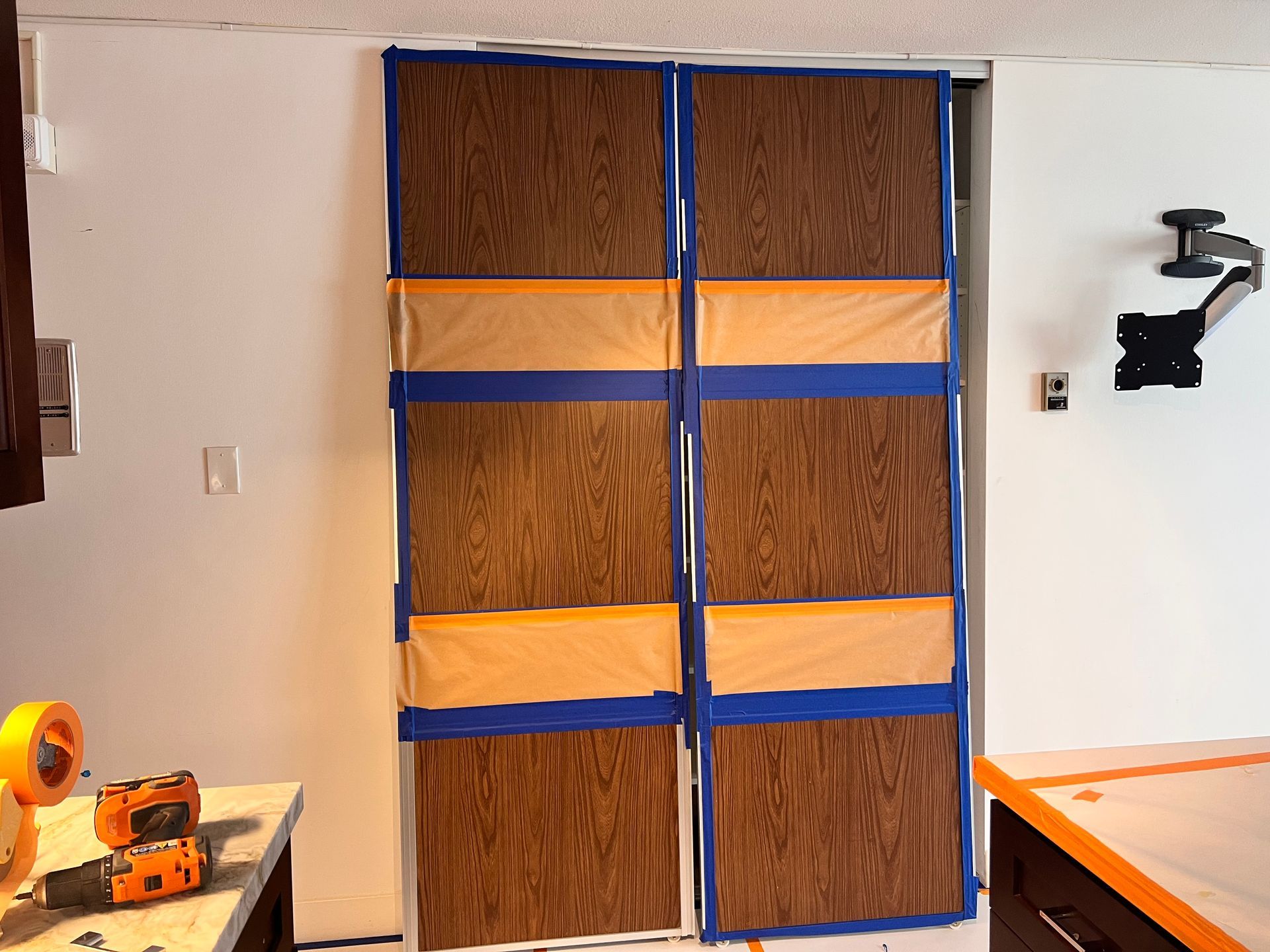 Taped-up wooden door panels in a room, with tools on a workbench and a wall-mounted device.