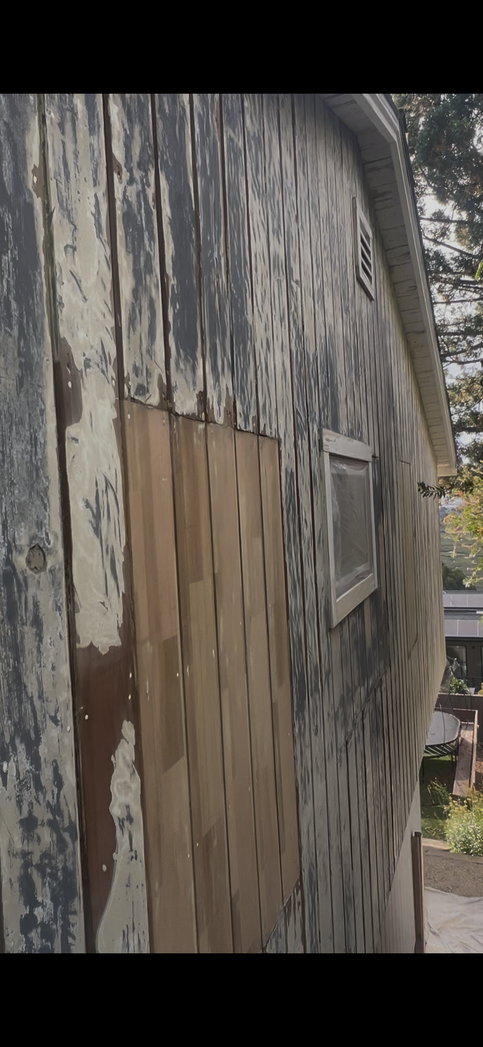 Weathered concrete wall with a boarded-up opening and peeling gray paint outdoors