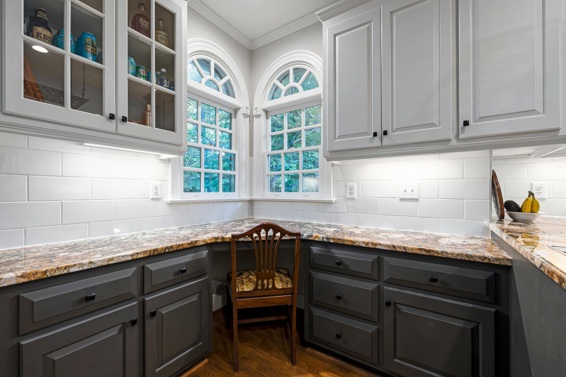 Modern kitchen with white cabinets, dark lower cabinets, granite countertops, and arched windows above the sink