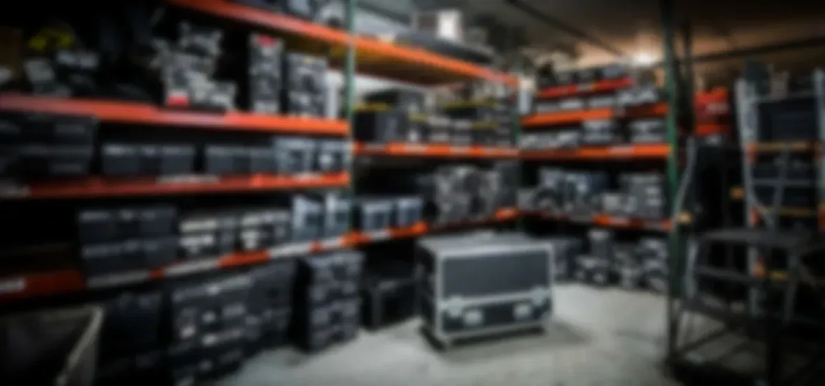 Shelves filled with black equipment in a warehouse. A large case sits on the floor.