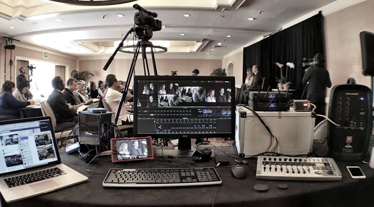 Video production control room with multiple monitors, cameras, and people working around a conference hall