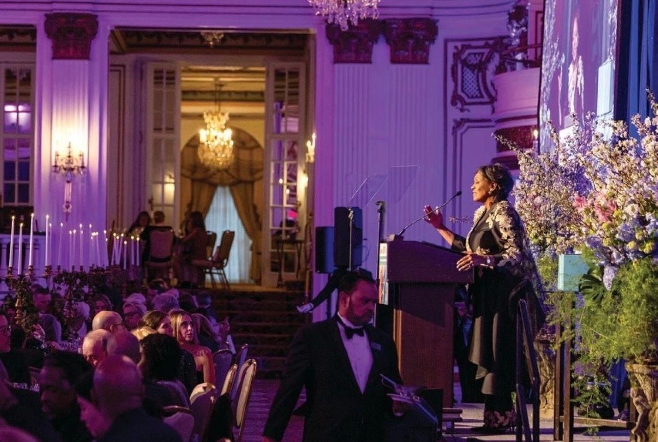 Musicians performing in a purple-lit grand hall with chandeliers and floral arrangements