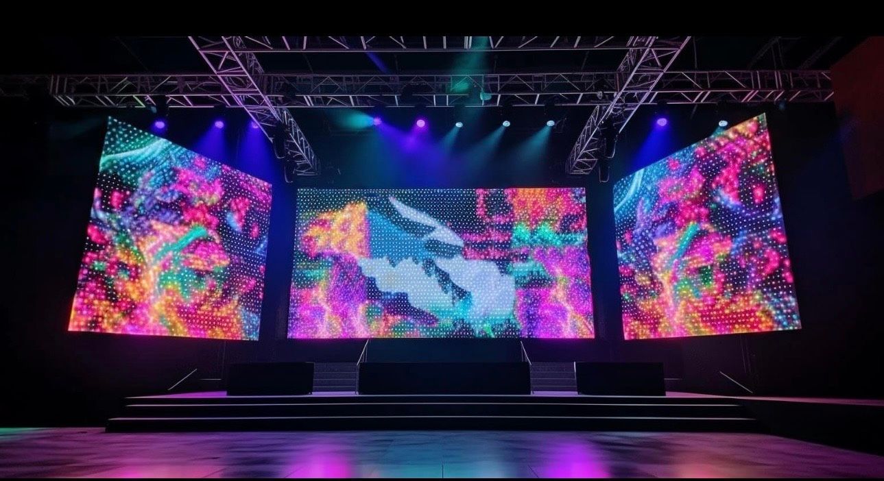 Empty concert stage with three large LED screens showing colorful abstract visuals and purple lighting