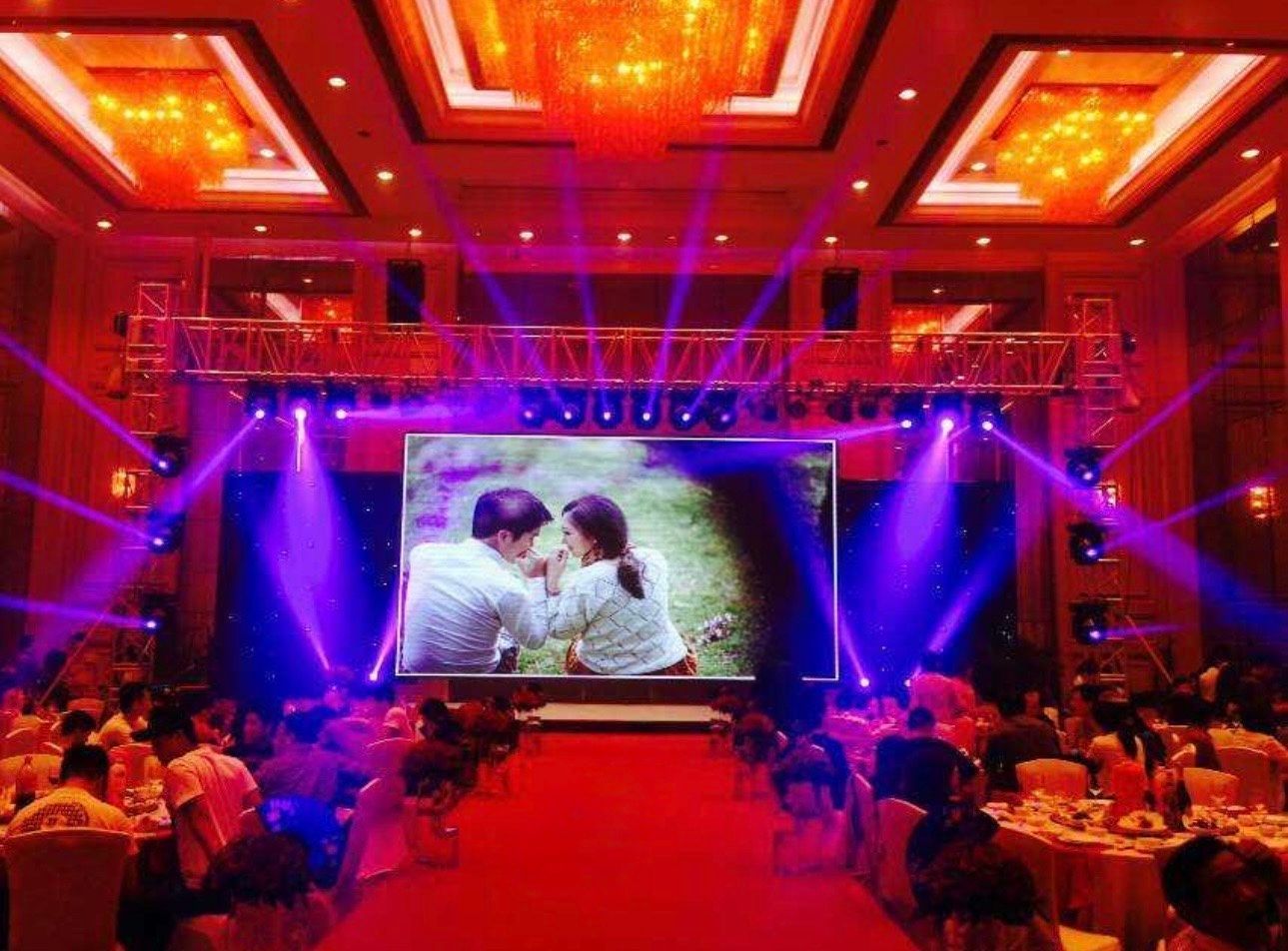 Elegant banquet hall with a large stage screen showing a couple, lit by red and purple spotlights