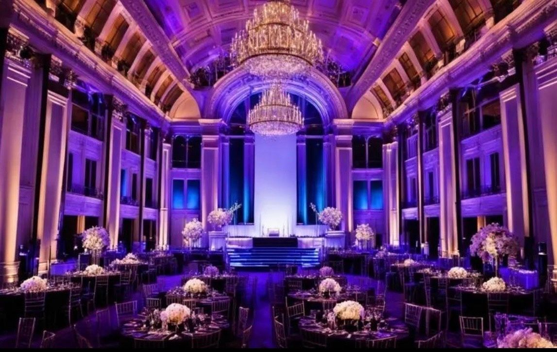 Grand ballroom with purple lighting, chandeliers, and formal dining tables set for an event
