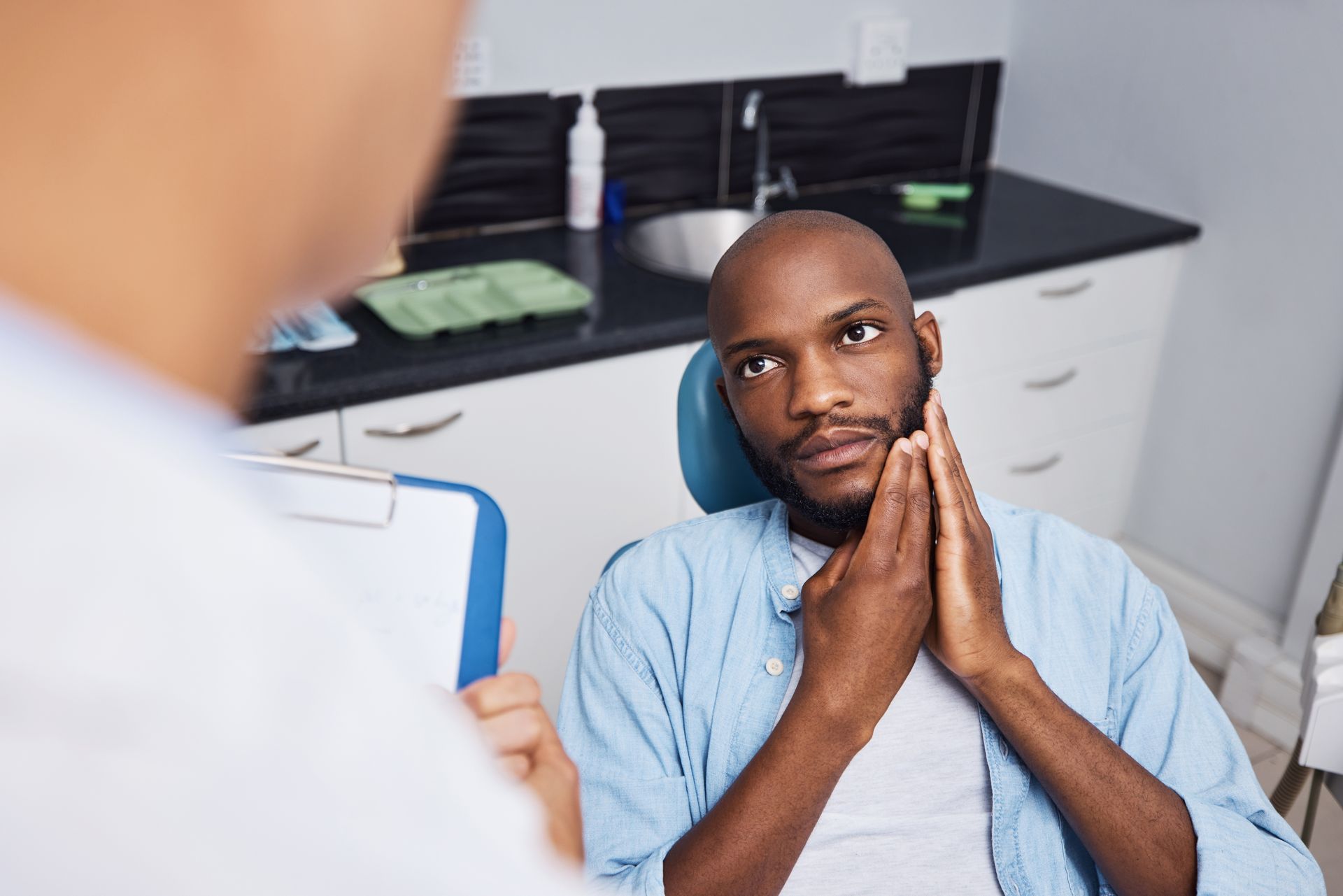 A dentist is showing a dental implant to a patient. A dental consultation showing a man sitting in a dental chair holding his jaw.