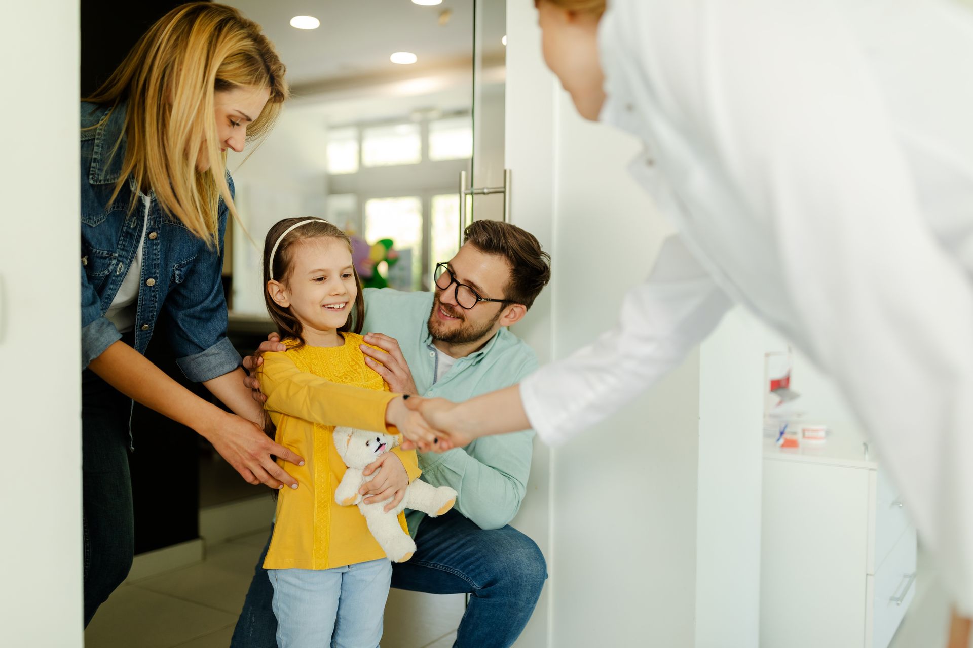 Family dentist greeting parents and their young daughter at a dental visit.
