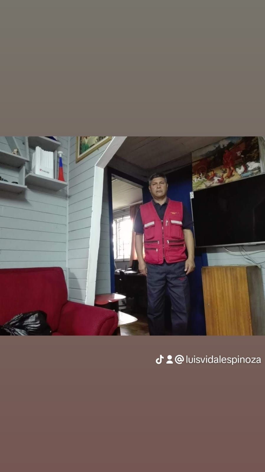 Un hombre con un chaleco rojo está de pie en una sala de estar.