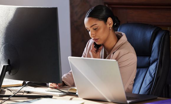 Person working at a desk with a laptop and large monitor, looking focused in an office chair.