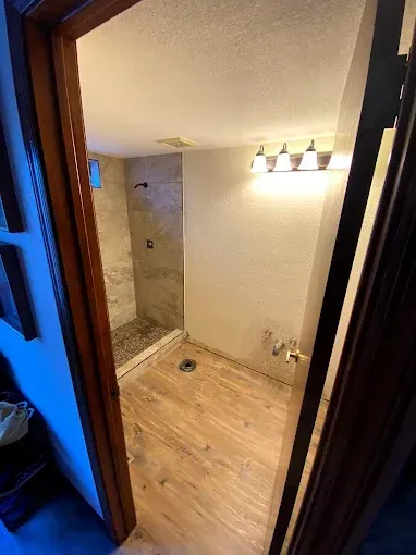 Bathroom interior with wood-look floor, stone tile shower, and wall-mounted light fixture.