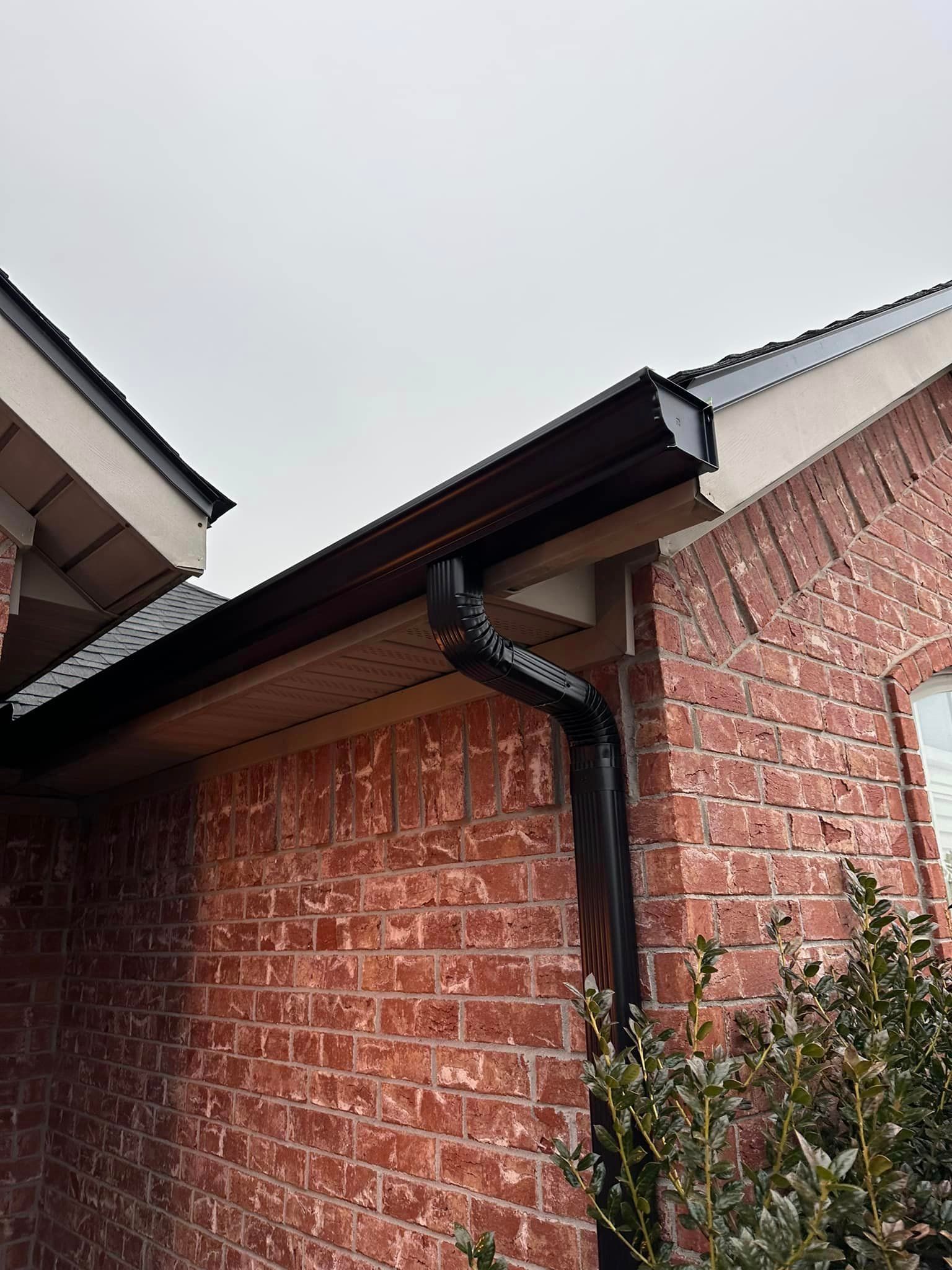 Brick house exterior with black gutter and downspout under an overcast sky