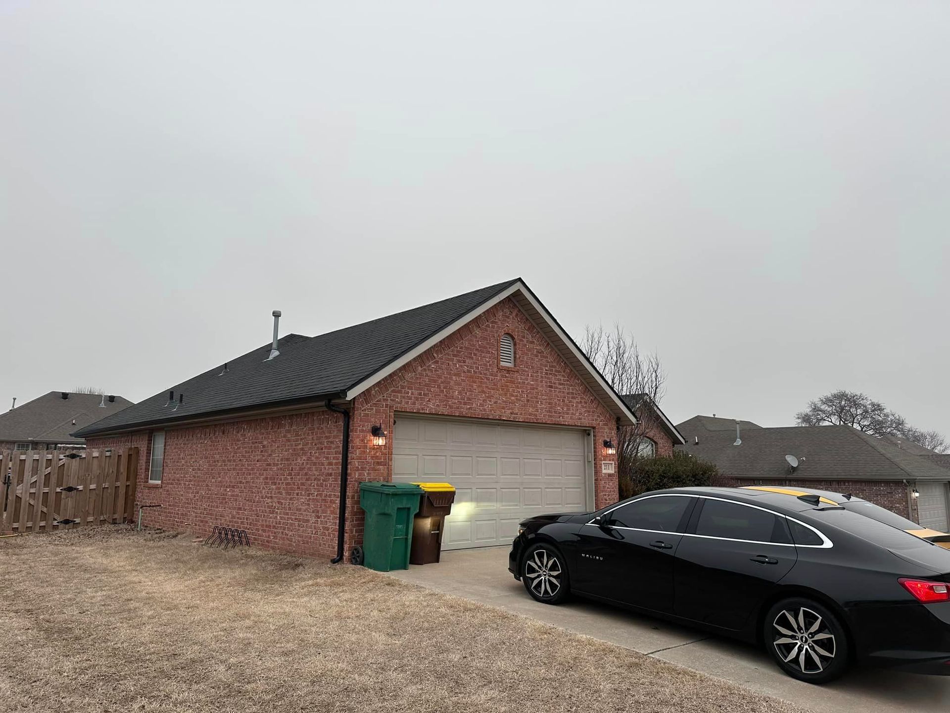 Brick garage with a black car parked in the driveway and trash bins beside the door