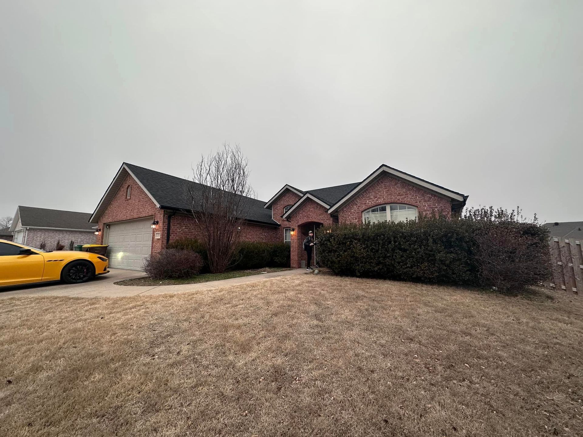 Brick suburban house with a yellow car parked in the driveway on a cloudy day