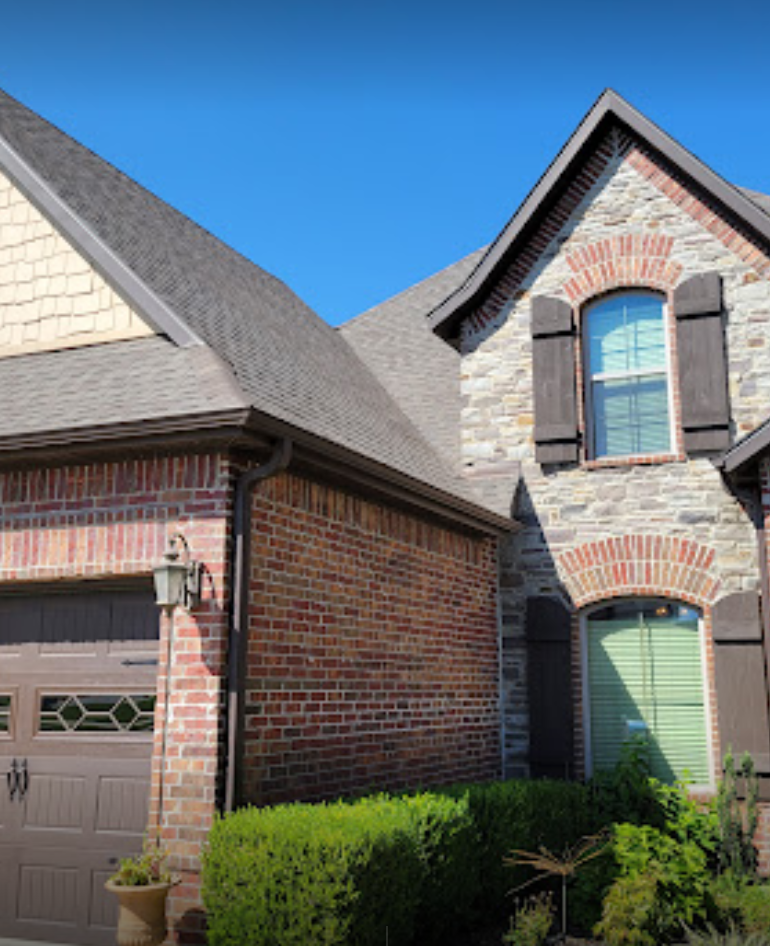 Brick suburban house exterior with gabled roof, garage, and arched windows under a blue sky