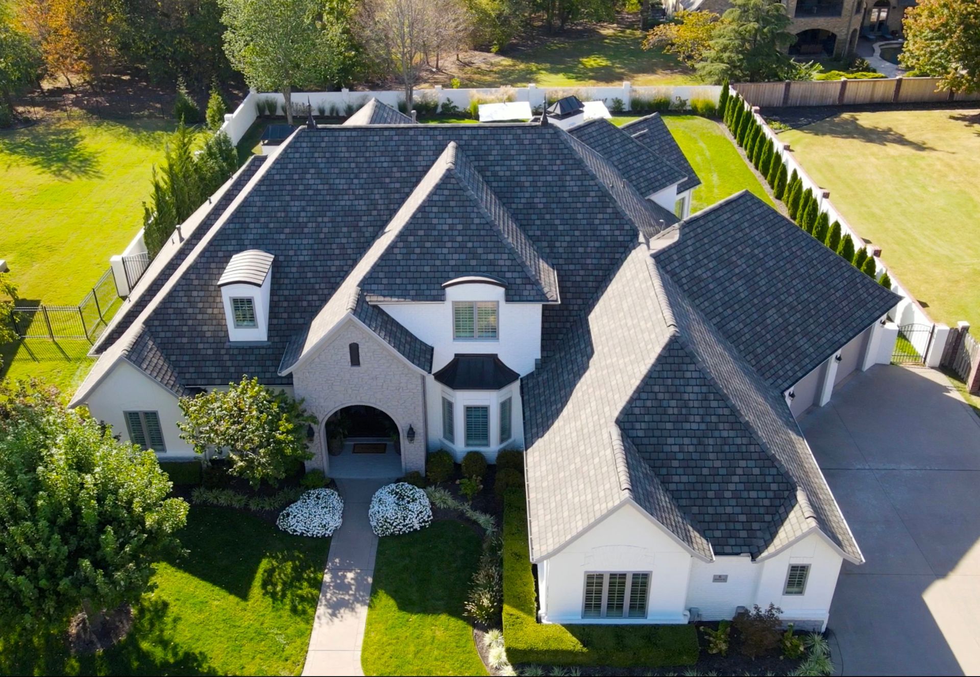 Aerial view of a large gray-roofed suburban house with a front lawn and driveway.