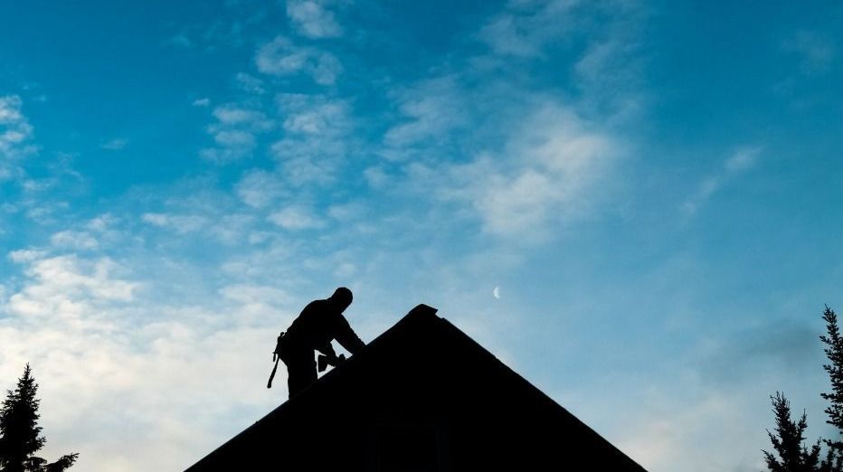 Silhouette of a person climbing a steep rooftop against a blue sky at dusk