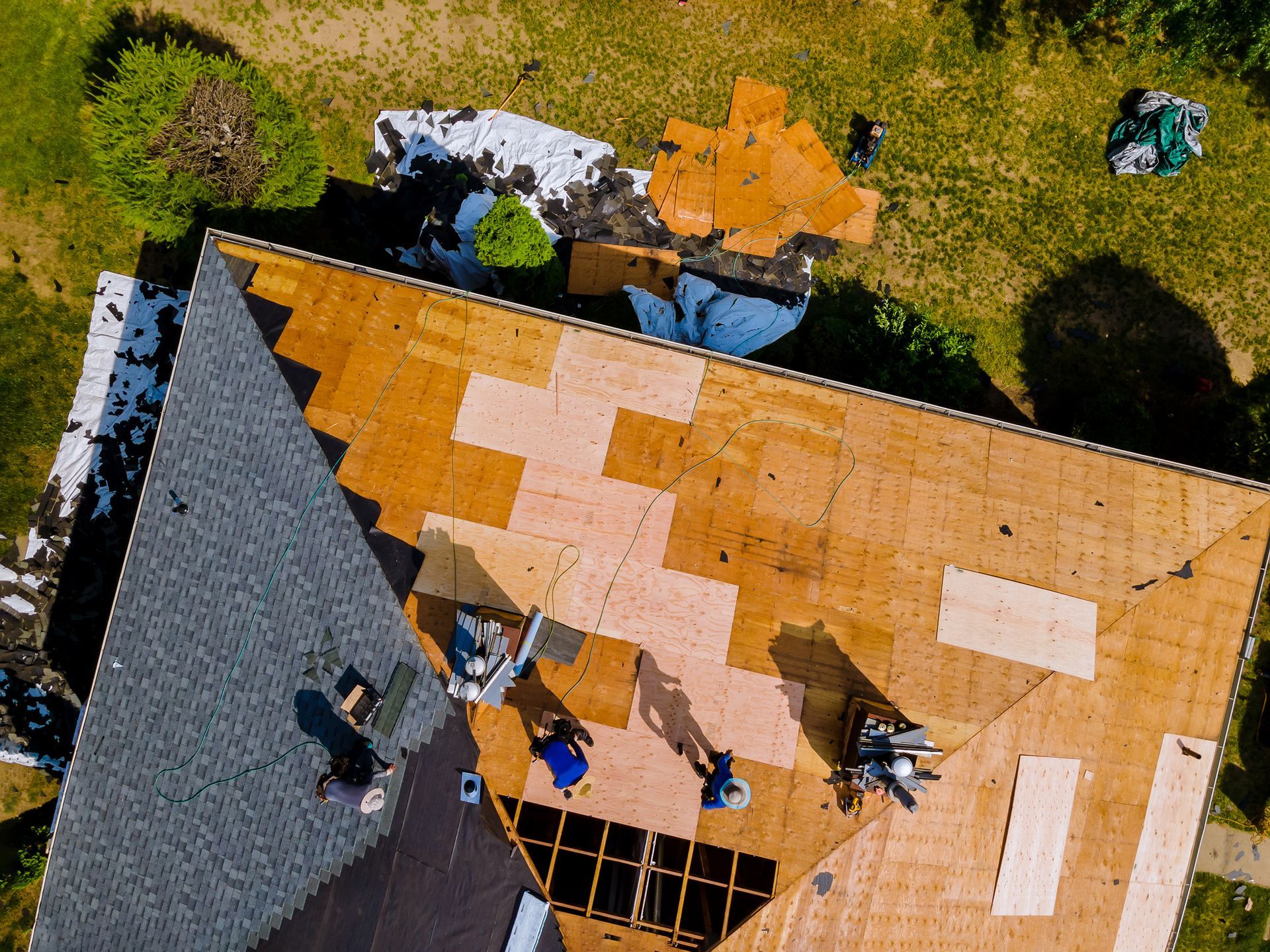 Aerial view of workers repairing an orange roof on a house amid grassy yard and trees