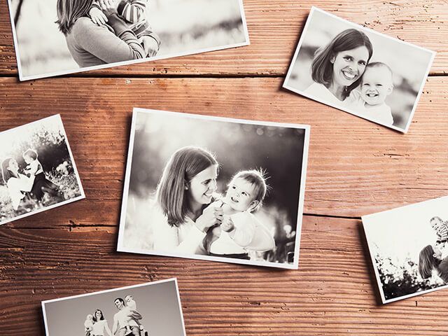 Black and white photos of mothers and babies scattered on a wooden surface.