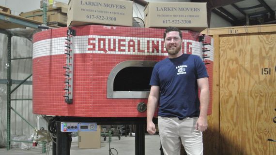 a man in a larkin shirt stands in front of a pizza oven
