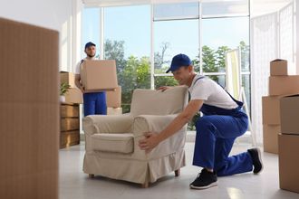 two men in blue overalls are moving a chair