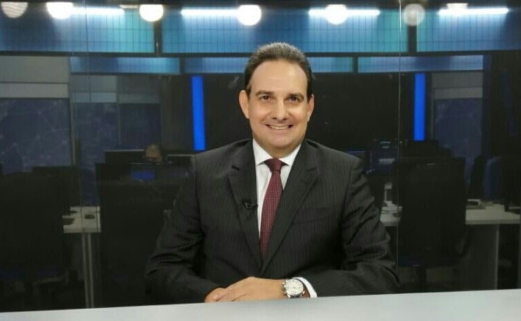 Um homem de terno e gravata está sorrindo enquanto está sentado em uma mesa