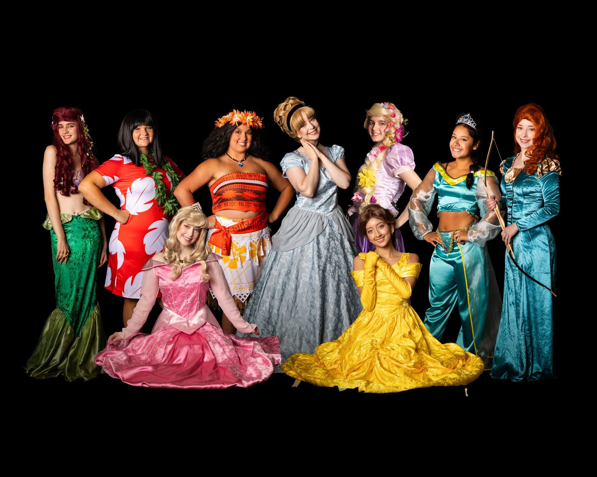 Group of costumed women posing as Disney princesses against a black backdrop.