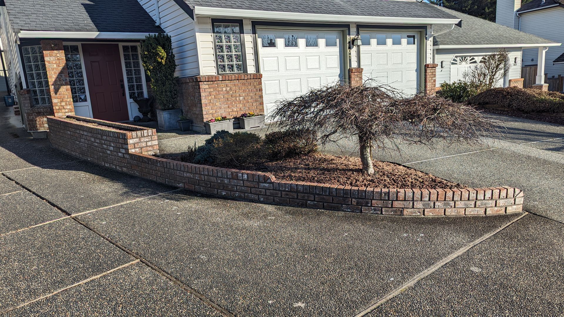 Brick house with attached garage and curved brick planter along a driveway in bright sunlight