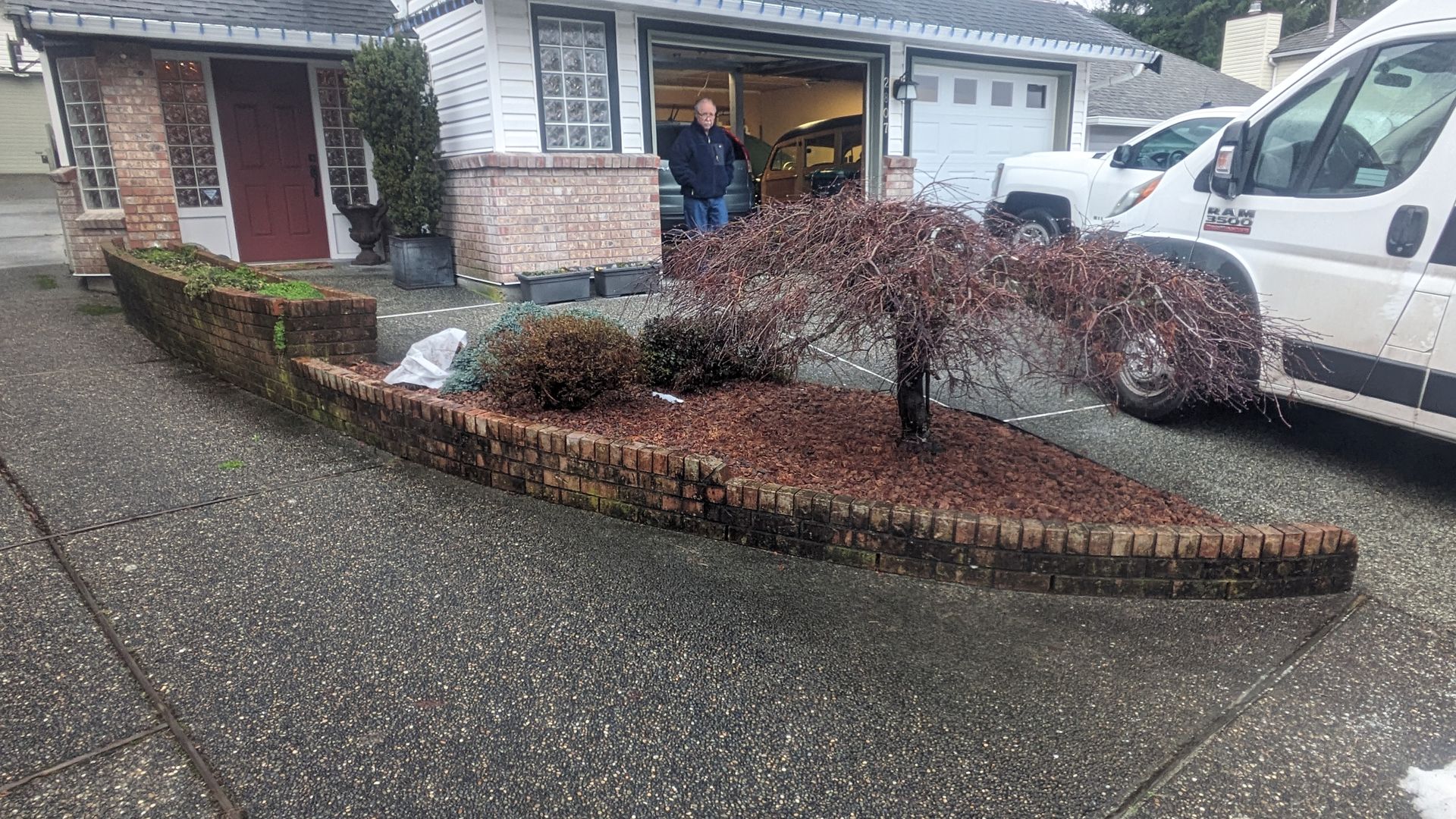 Rainy suburban driveway with a landscaped island and parked vehicles beside a house