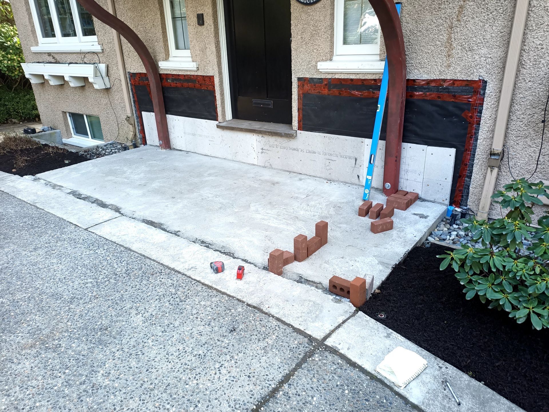Front porch with fresh concrete slab and brick edging under construction beside a house entry.