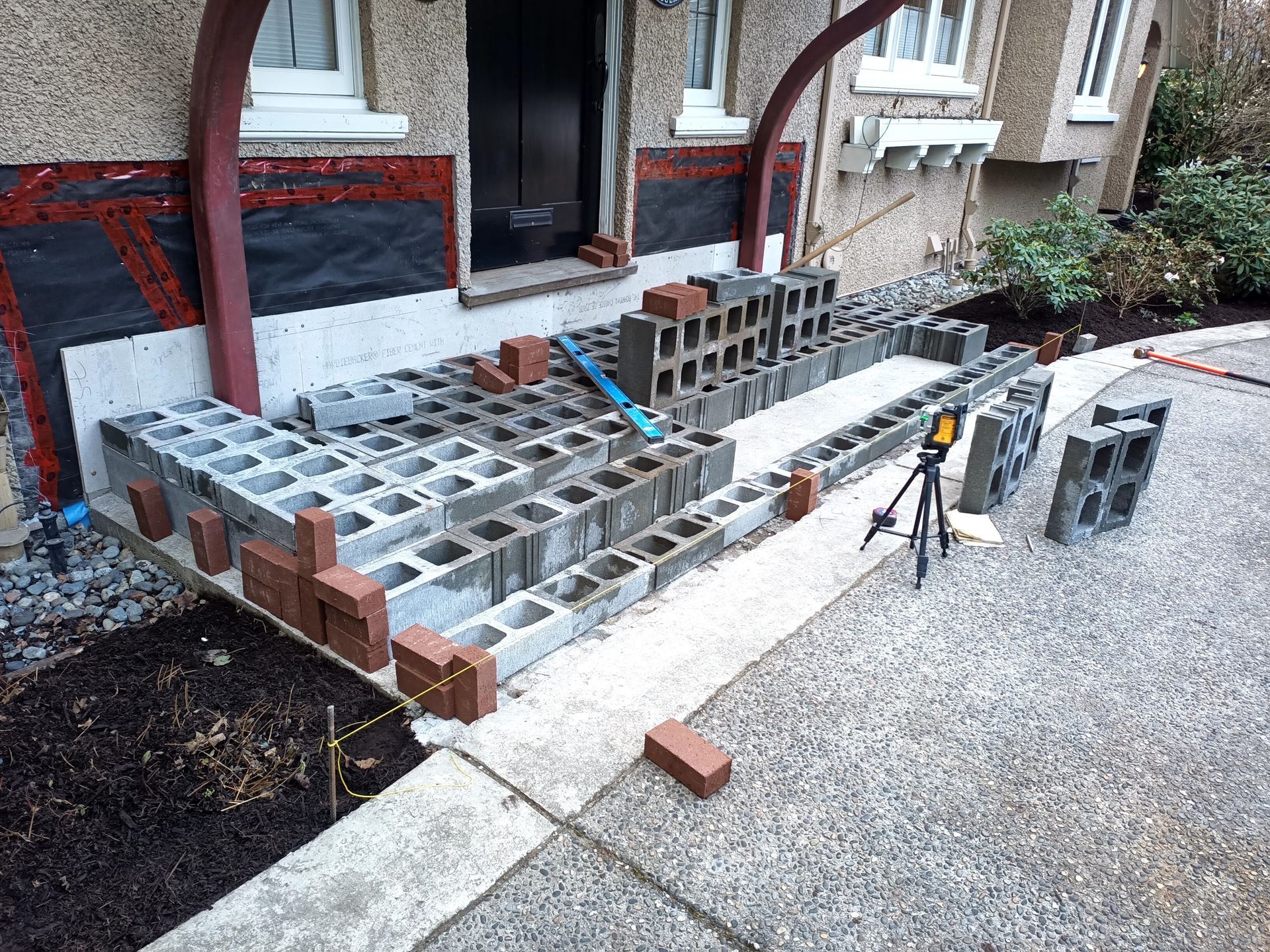 Partially built brick steps and a small patio beside a house, with tools and gravel around the work area