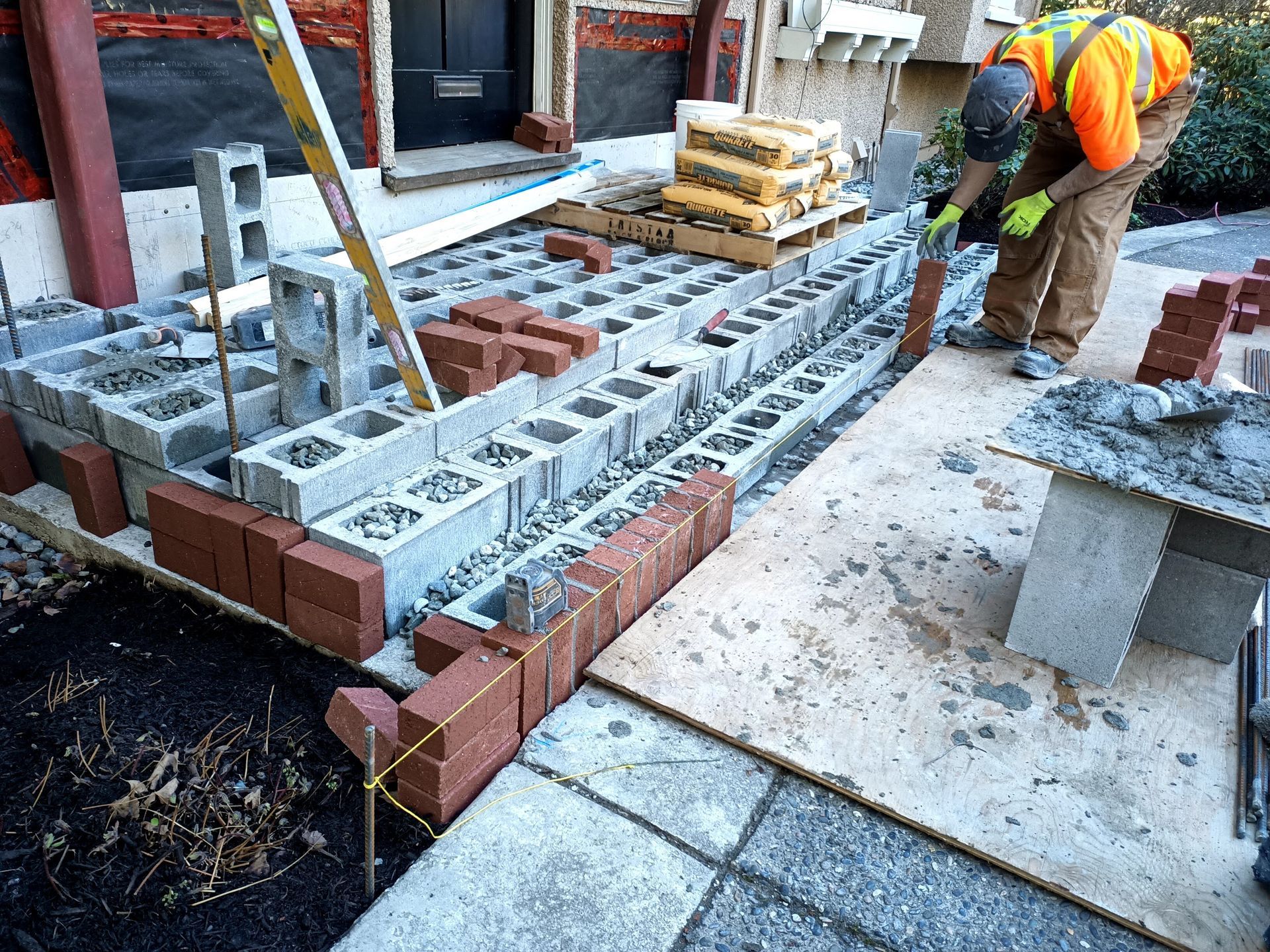 Workers laying concrete blocks at a construction site beside a building entrance