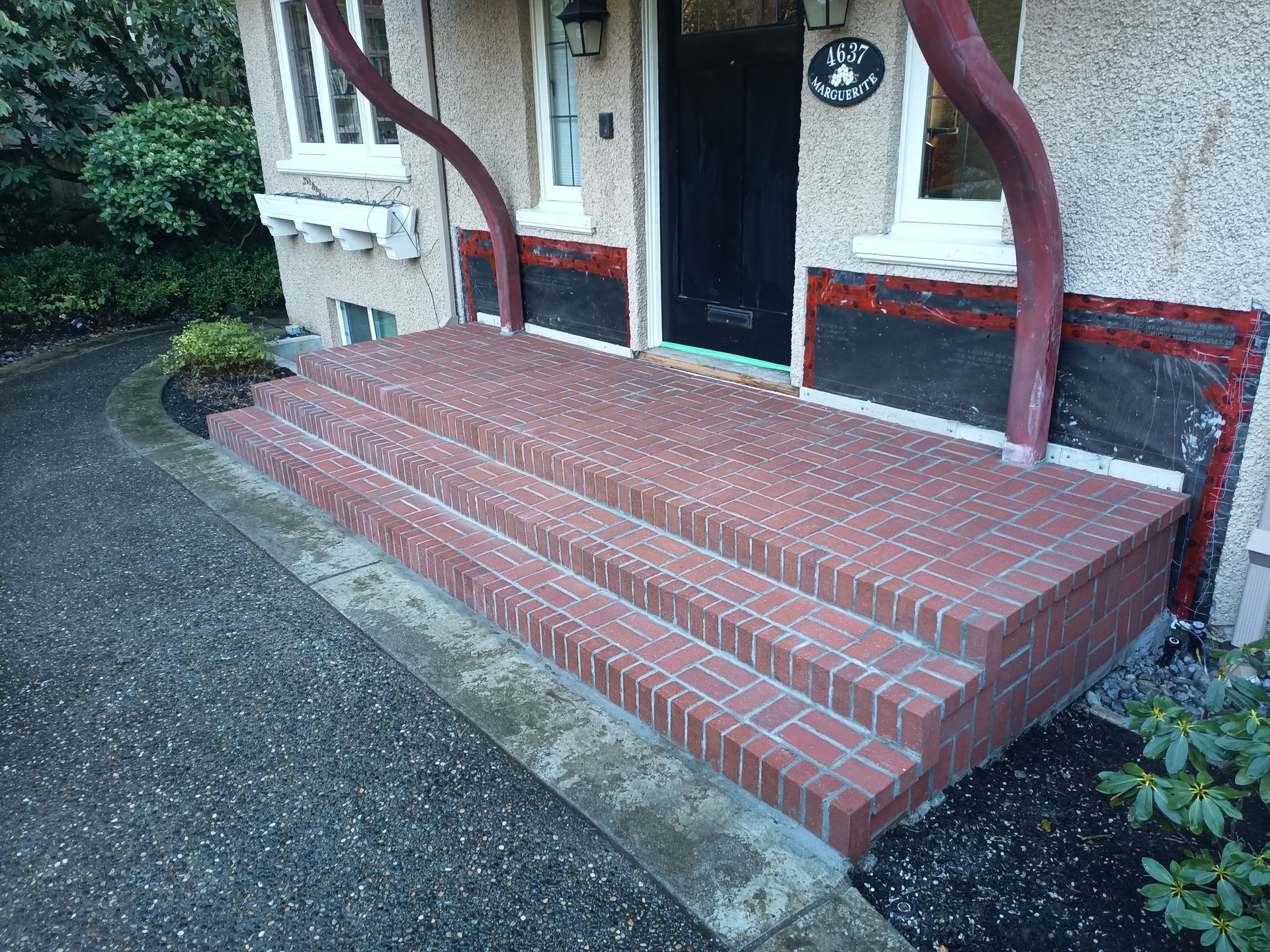 Brick front steps leading to a doorway with red handrails and a small porch at a house entrance