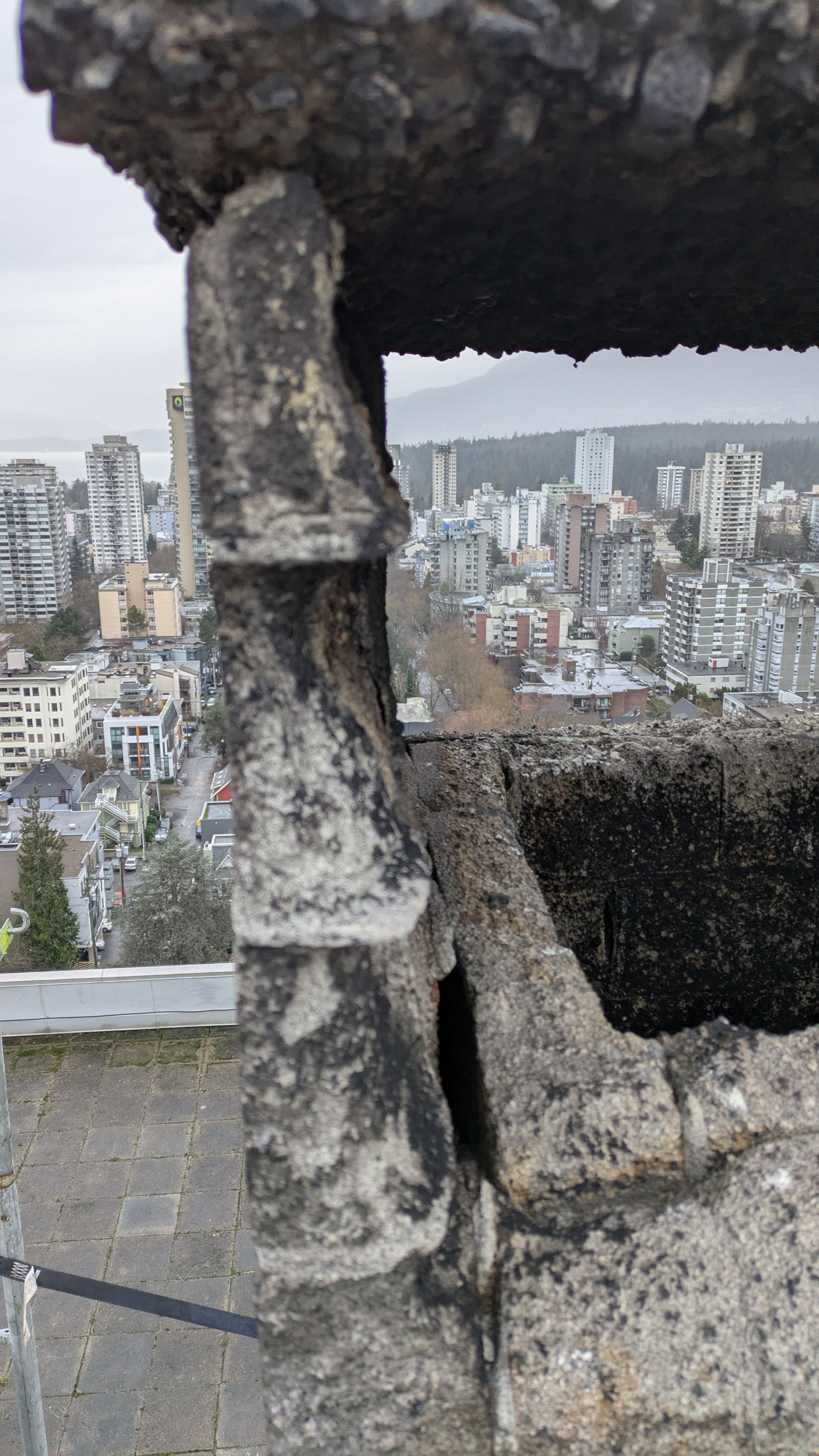 Damaged concrete ledge overlooking a dense city skyline under cloudy sky