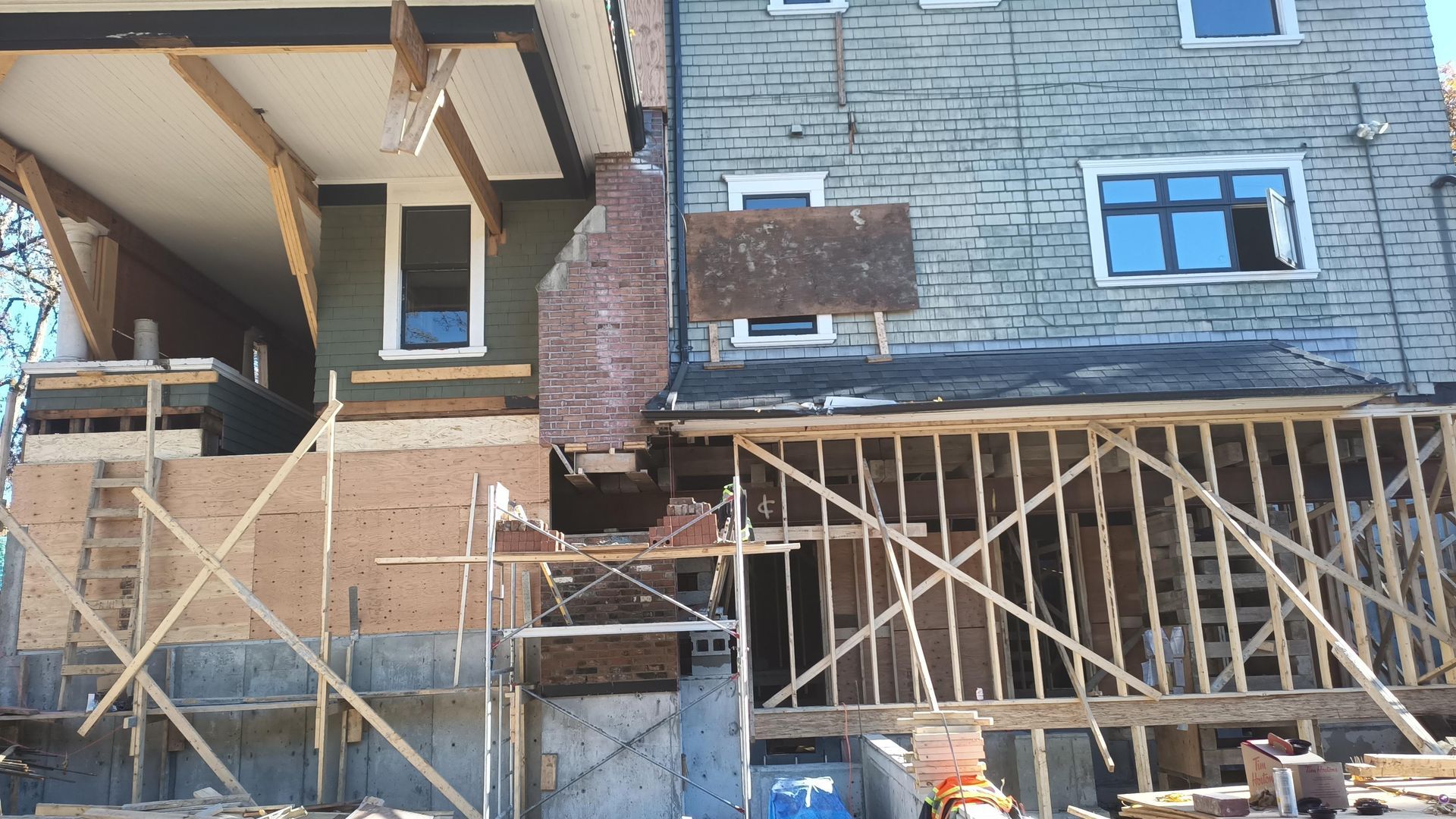 Partially built house with scaffolding, exposed brick and wood framing, and unfinished stone siding